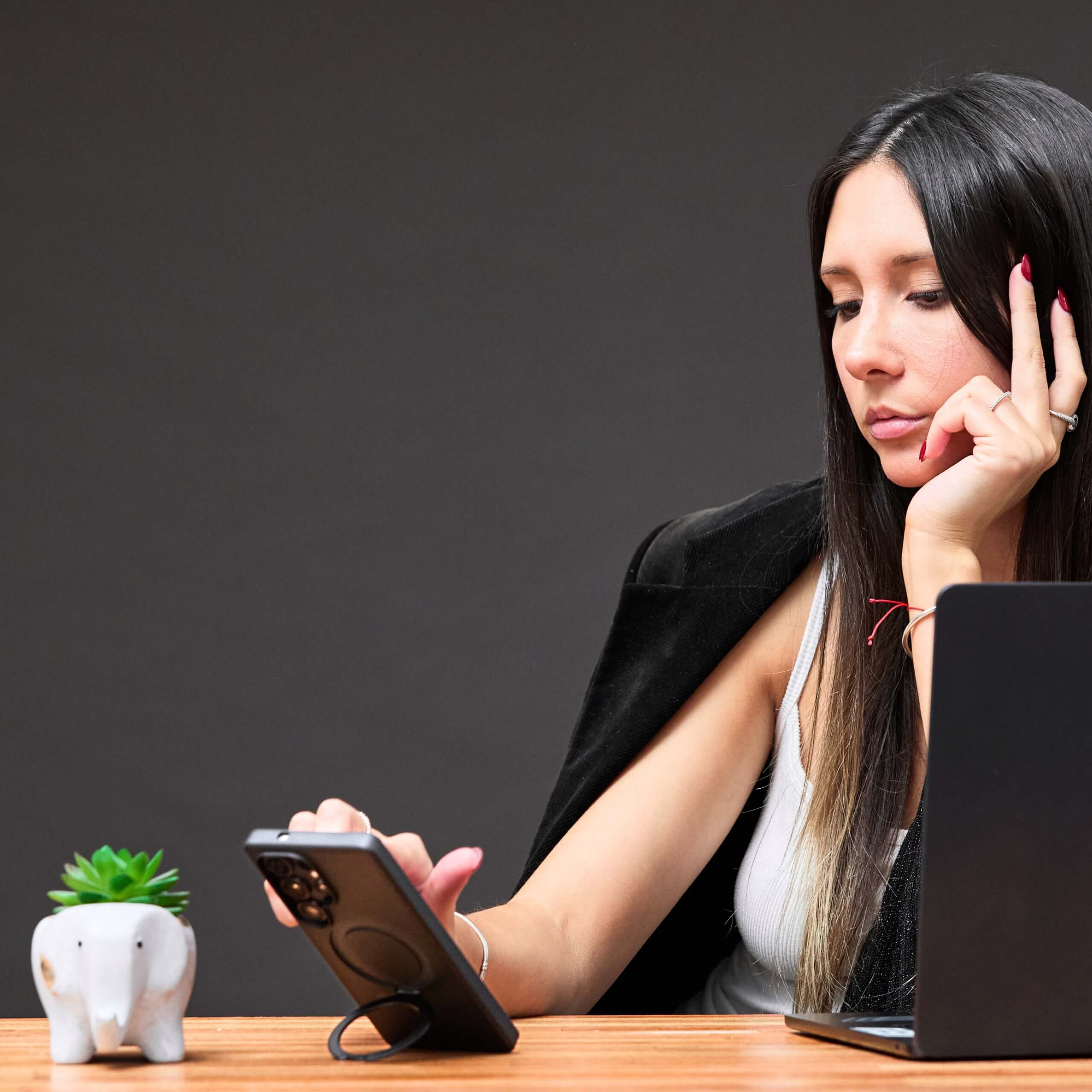 Mujer usando funda con aro magnético, apoyada en la mesa mientras mira el teléfono Samsung S25 Ultra. #color_negro