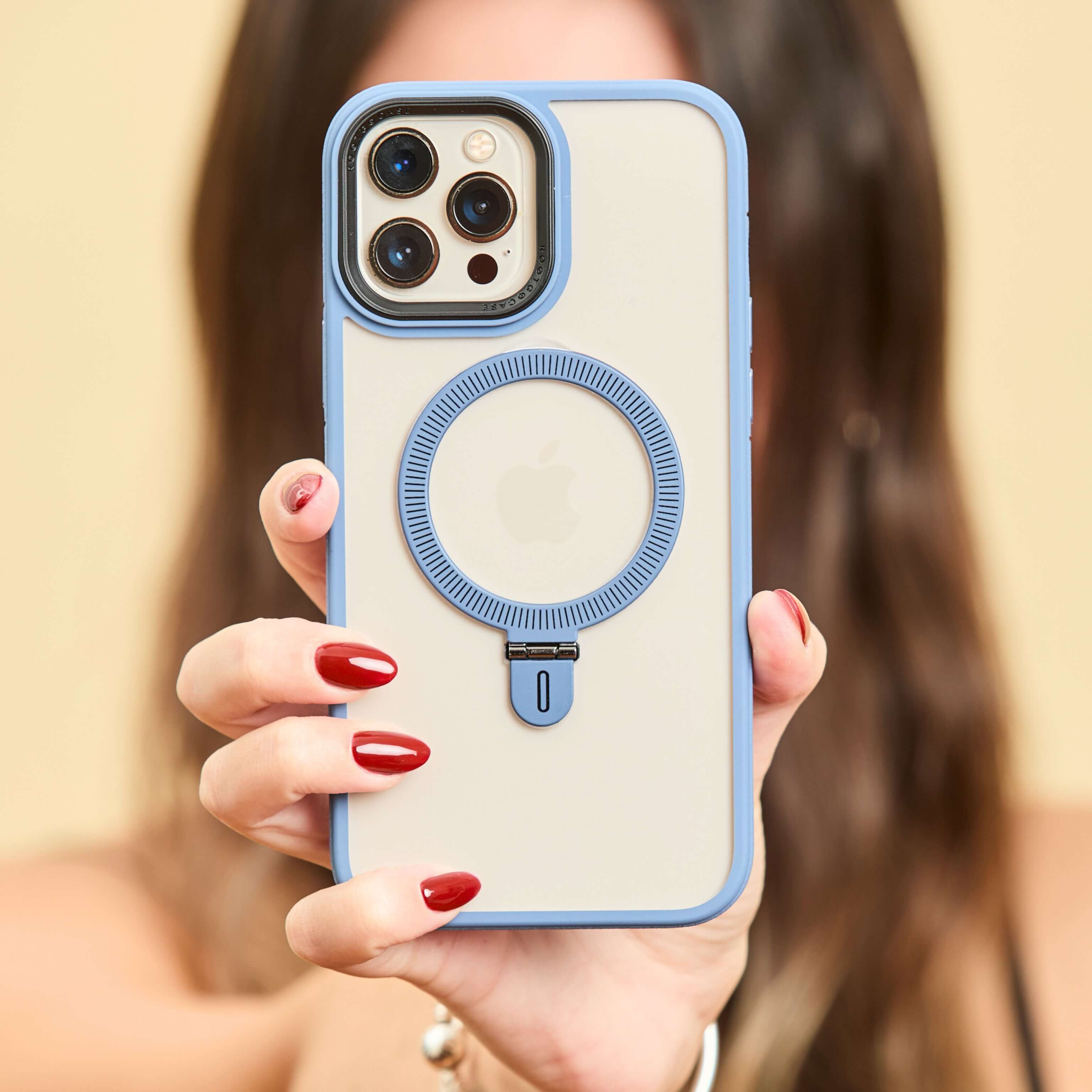 Primer plano de funda transparente con bordes azules y anillo trasero, sostenida por una mujer con uñas rojas. #color_azul