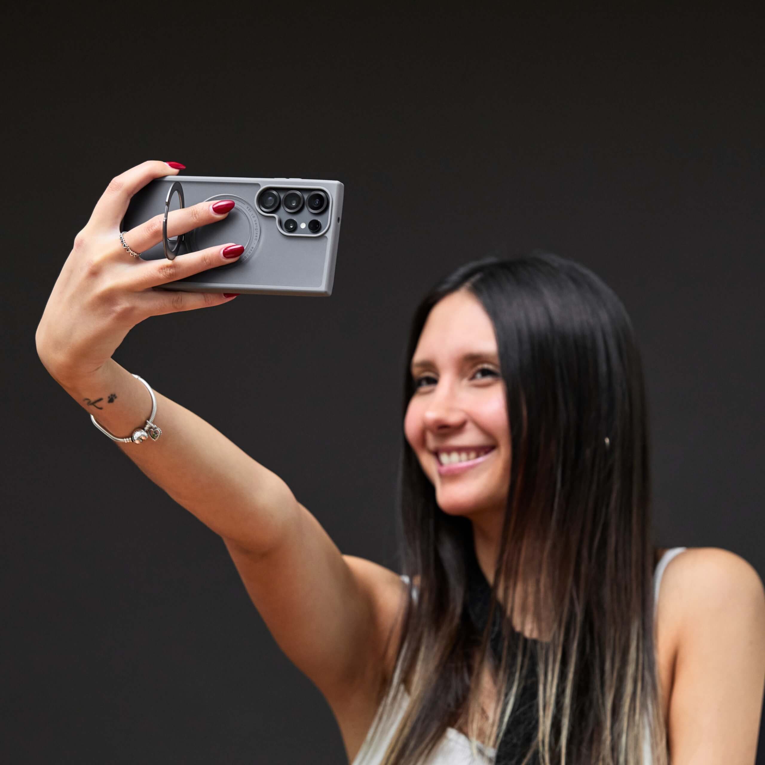 Mujer sacándose una selfie con el teléfono S25 de Samsung protegido por funda con aro magnético. #color_gris