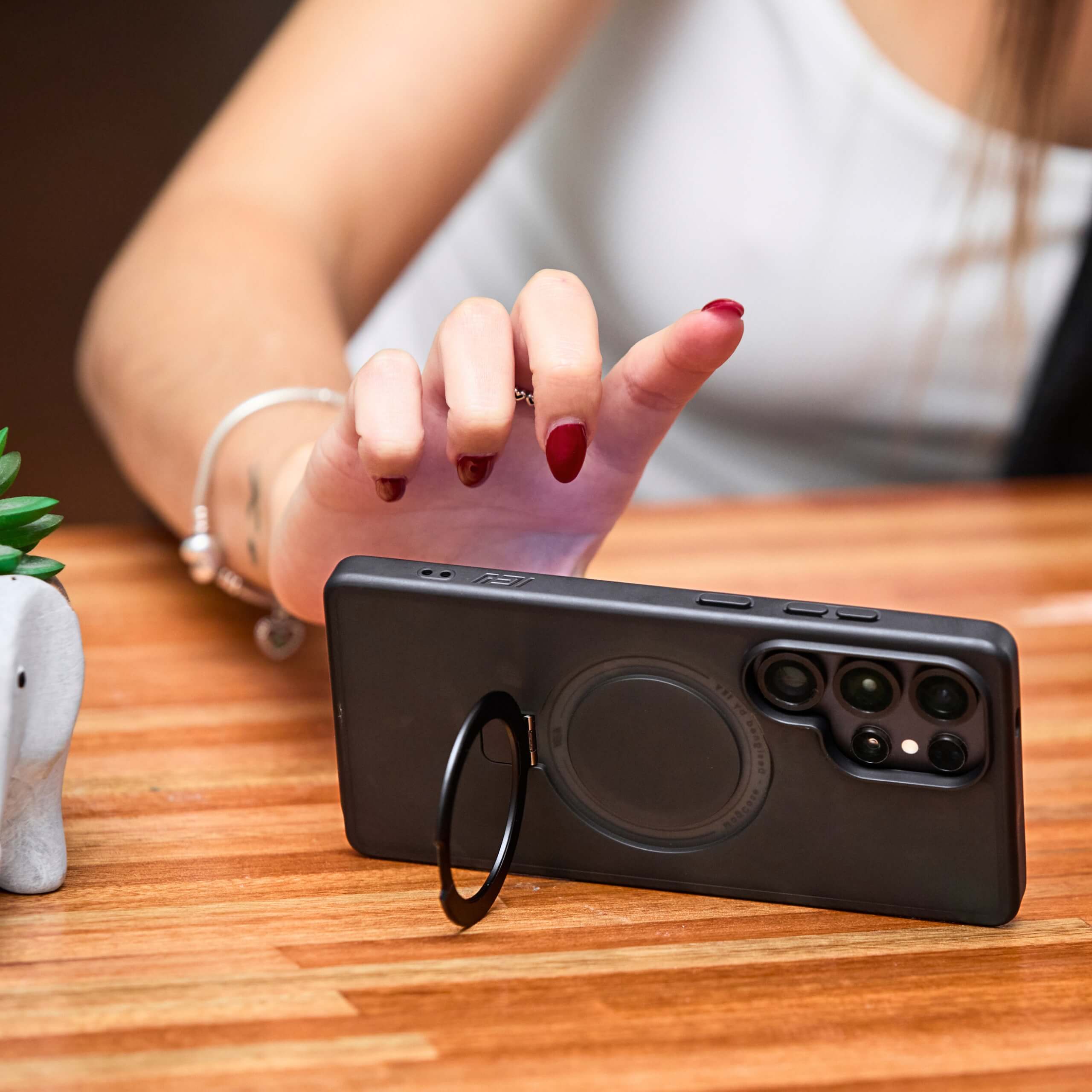 Mujer tocando la pantalla del teléfono apoyado en la mesa con funda y aro magnético. #color_negro