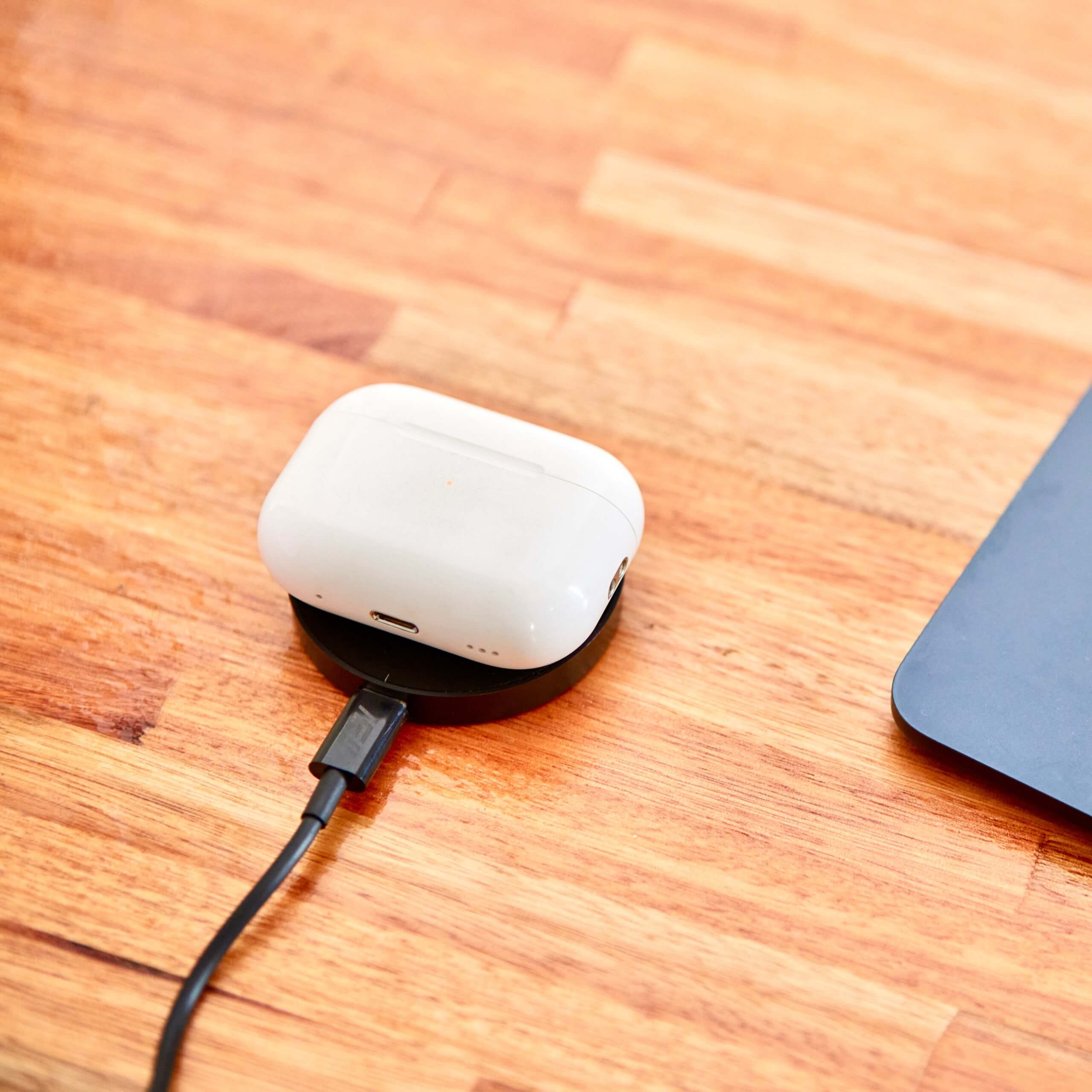 Audífonos inalámbricos tipo AirPods cargando sobre base inalámbrica IEY en escritorio de madera.