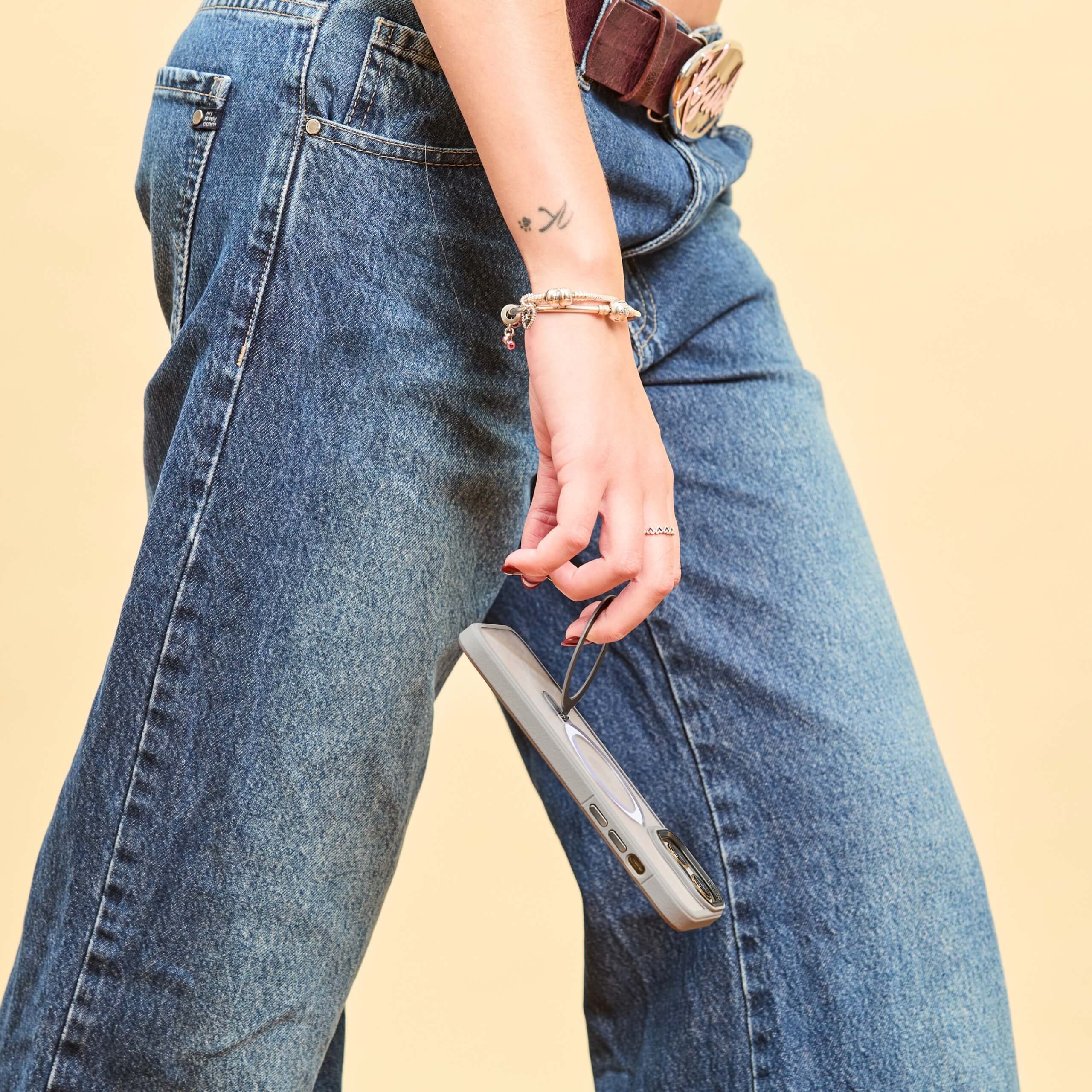 Mujer caminando con funda de iPhone transparente y bordes grises colgando de su dedo, usando el anillo trasero como agarre #color_gris
