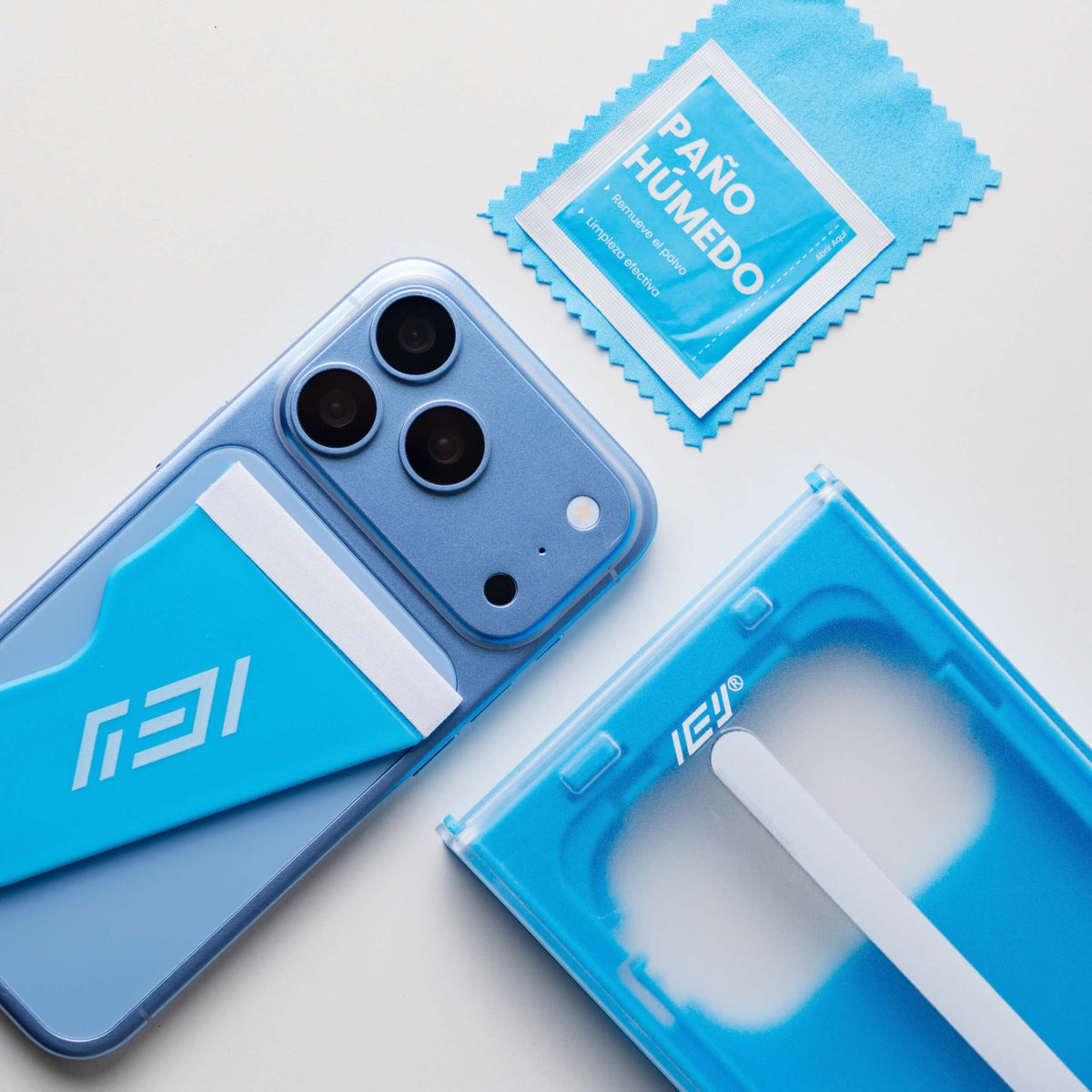 Detalle del kit ApplyFit™ de IEY® junto a un iPhone, con aplicador de vidrio templado, paño húmedo y microfibra de limpieza.