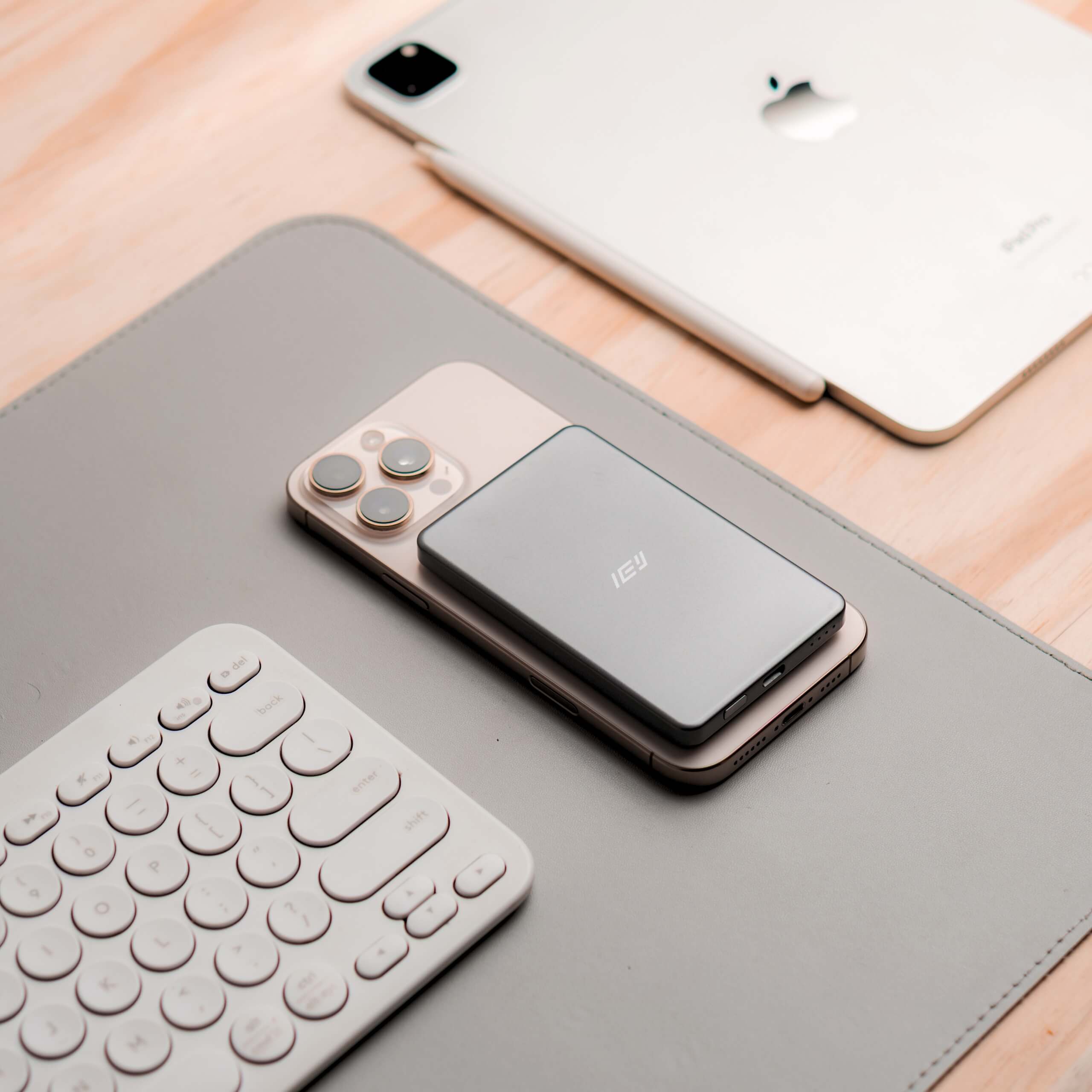 Power Bank MagSafe ultrafino IEY en color gris sobre iPhone, junto a teclado inalámbrico y iPad, diseño minimalista en escritorio. #color_gris azulado