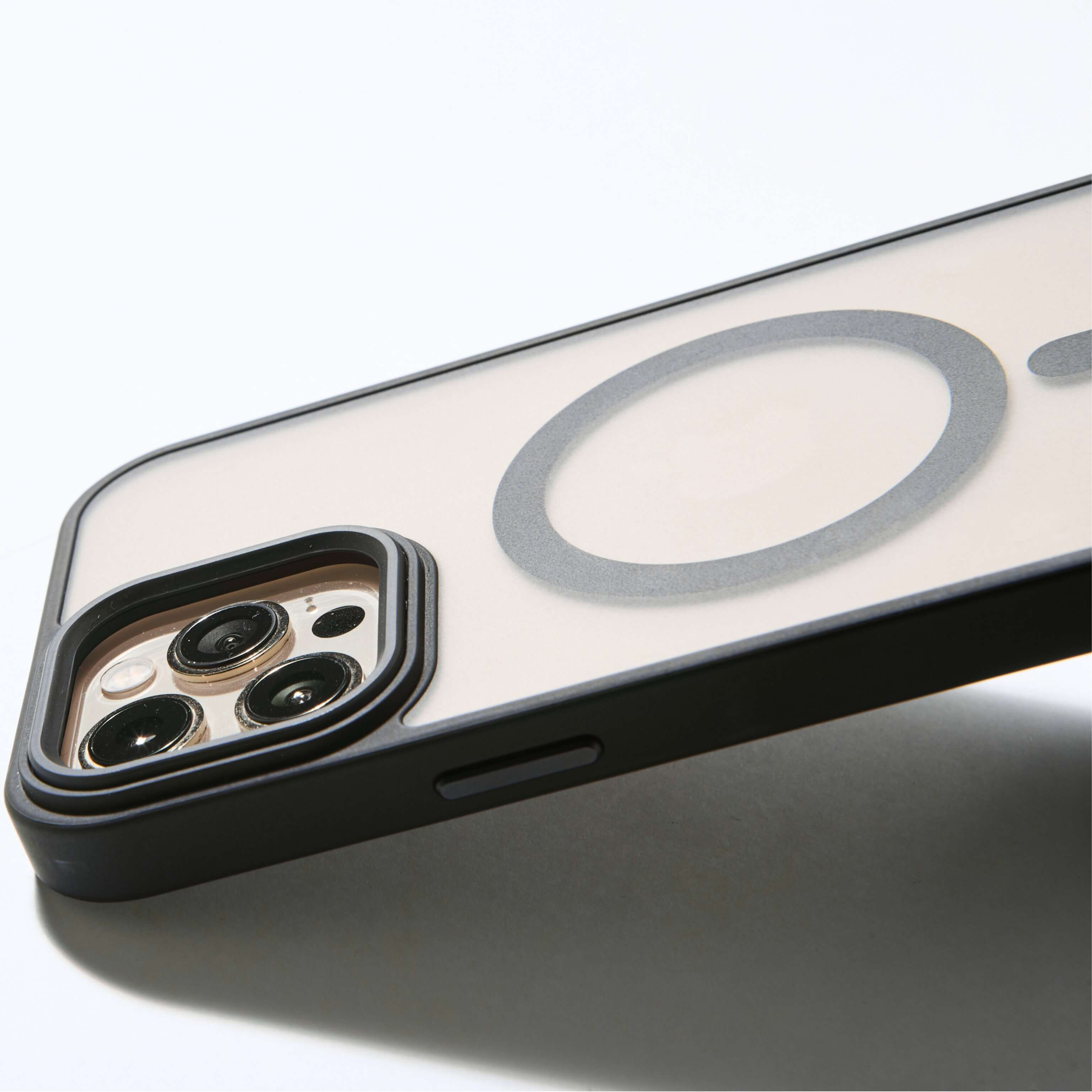 Funda MagSafe negra para iPhone apoyada de lado, con aro imantado visible y bordes elevados de protección para cámara
