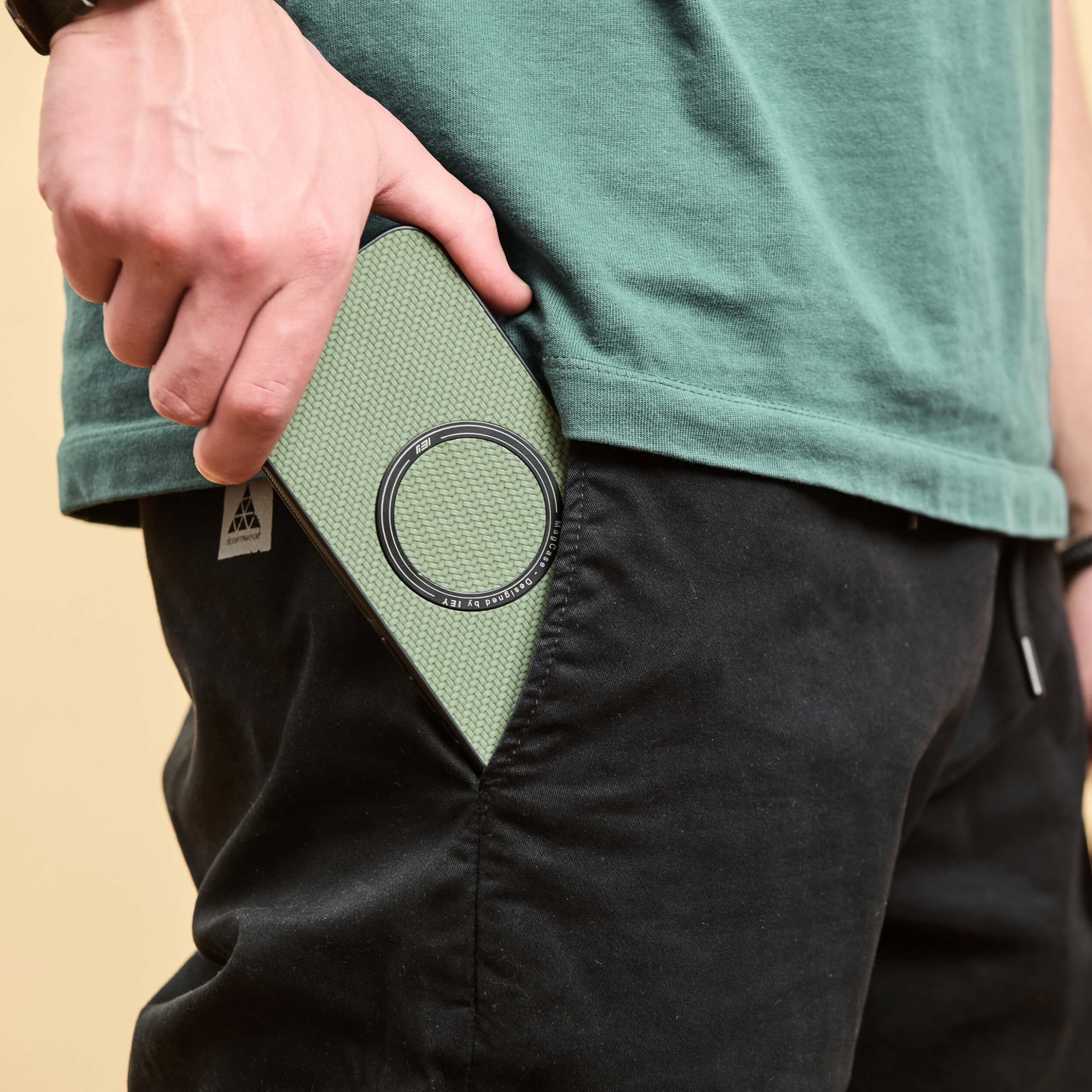 Hombre guardando un iPhone con funda MagSafe verde en el bolsillo trasero.