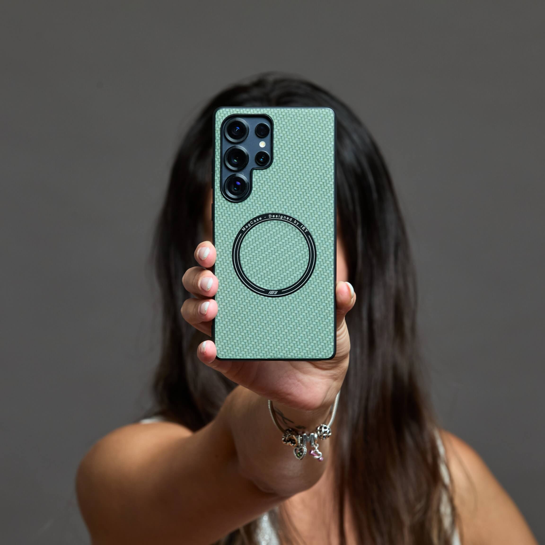 Funda MagSafe Samsung verde con textura de carbono, sostenida en la mano de una mujer #color_verde