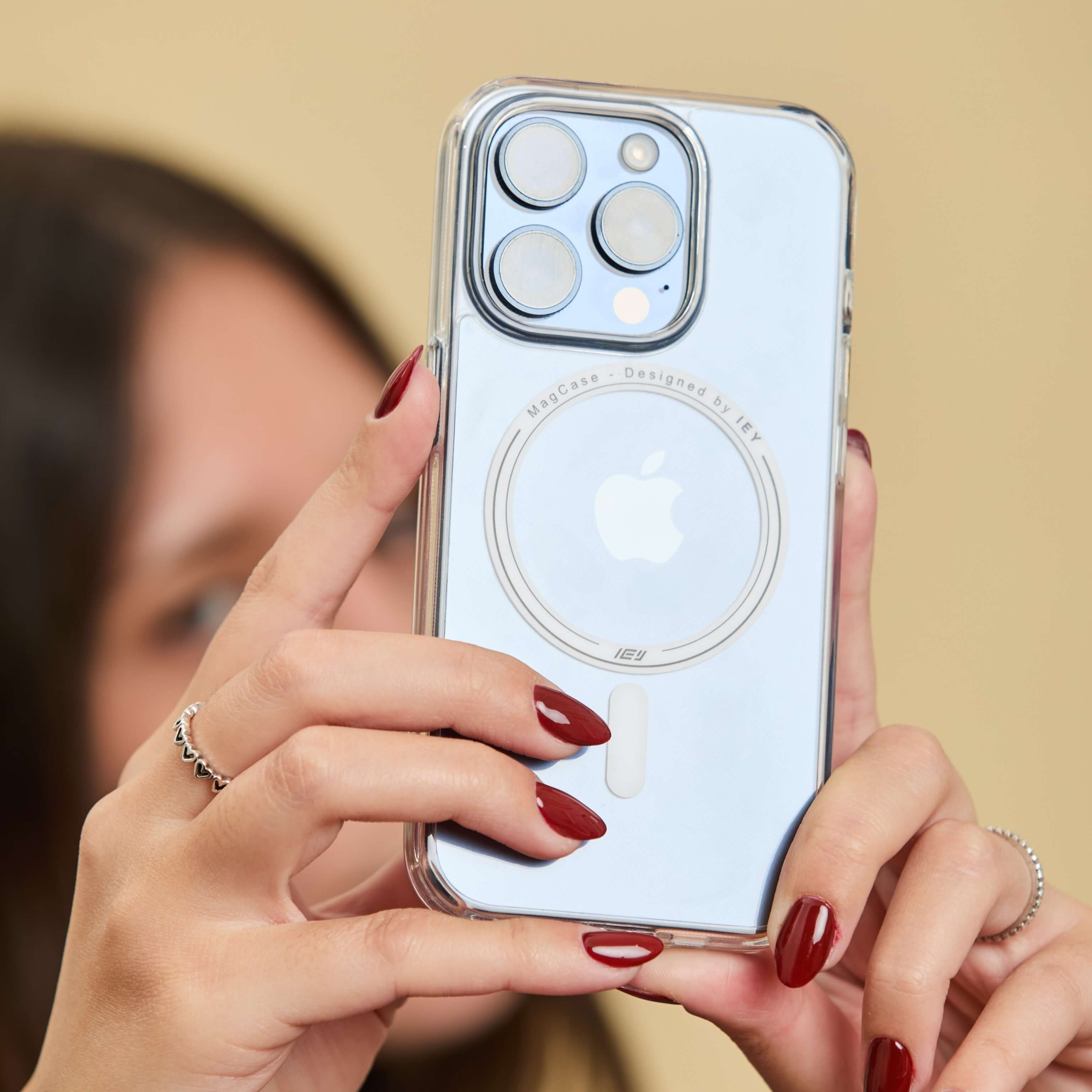 Funda MagSafe transparente en iPhone sostenido con ambas manos, detalle del aro imantado y logo IEY visible en primer plano