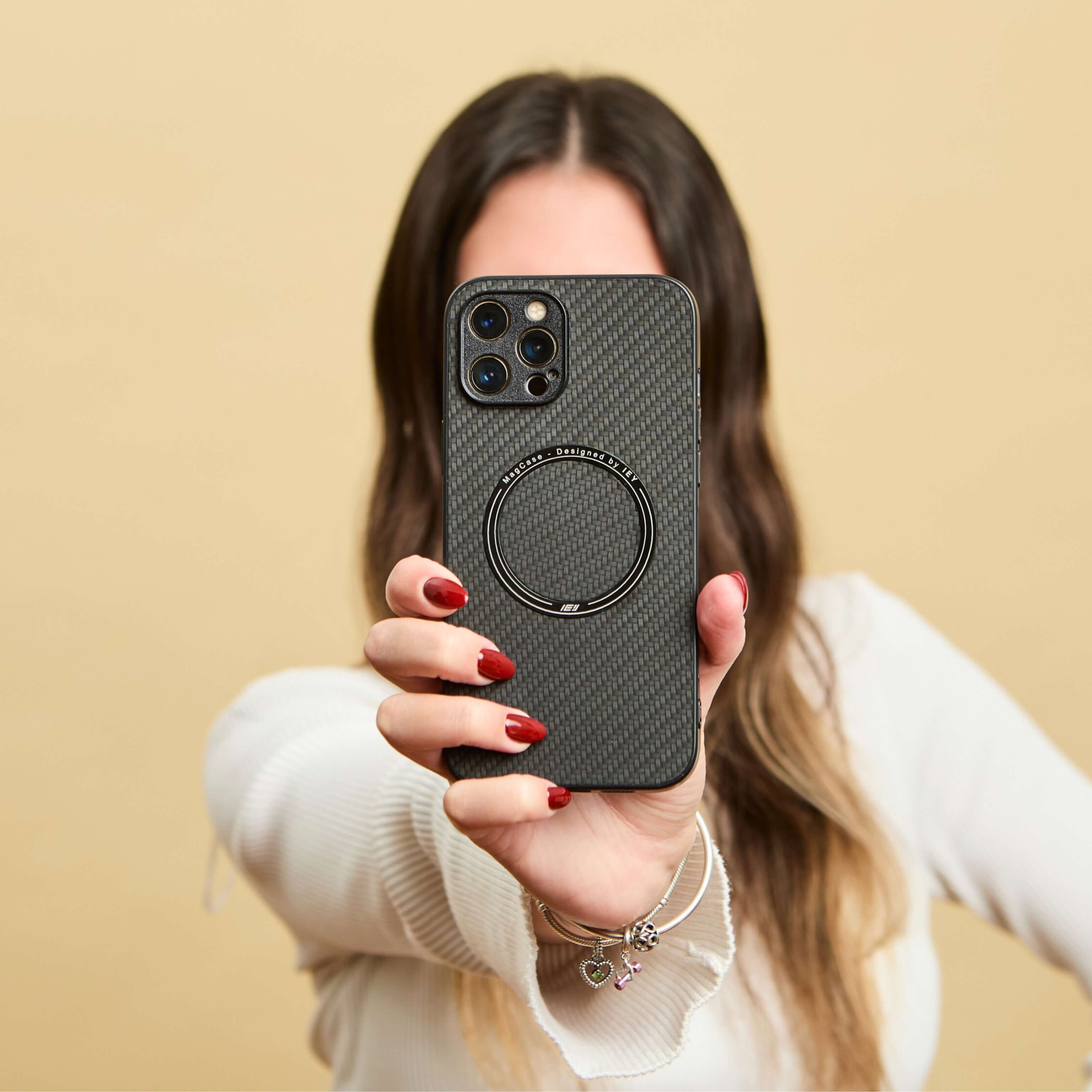 Mujer con suéter blanco sosteniendo un iPhone con funda MagSafe de fibra de carbono frente a la cámara, en gesto de selfie #color_negro
