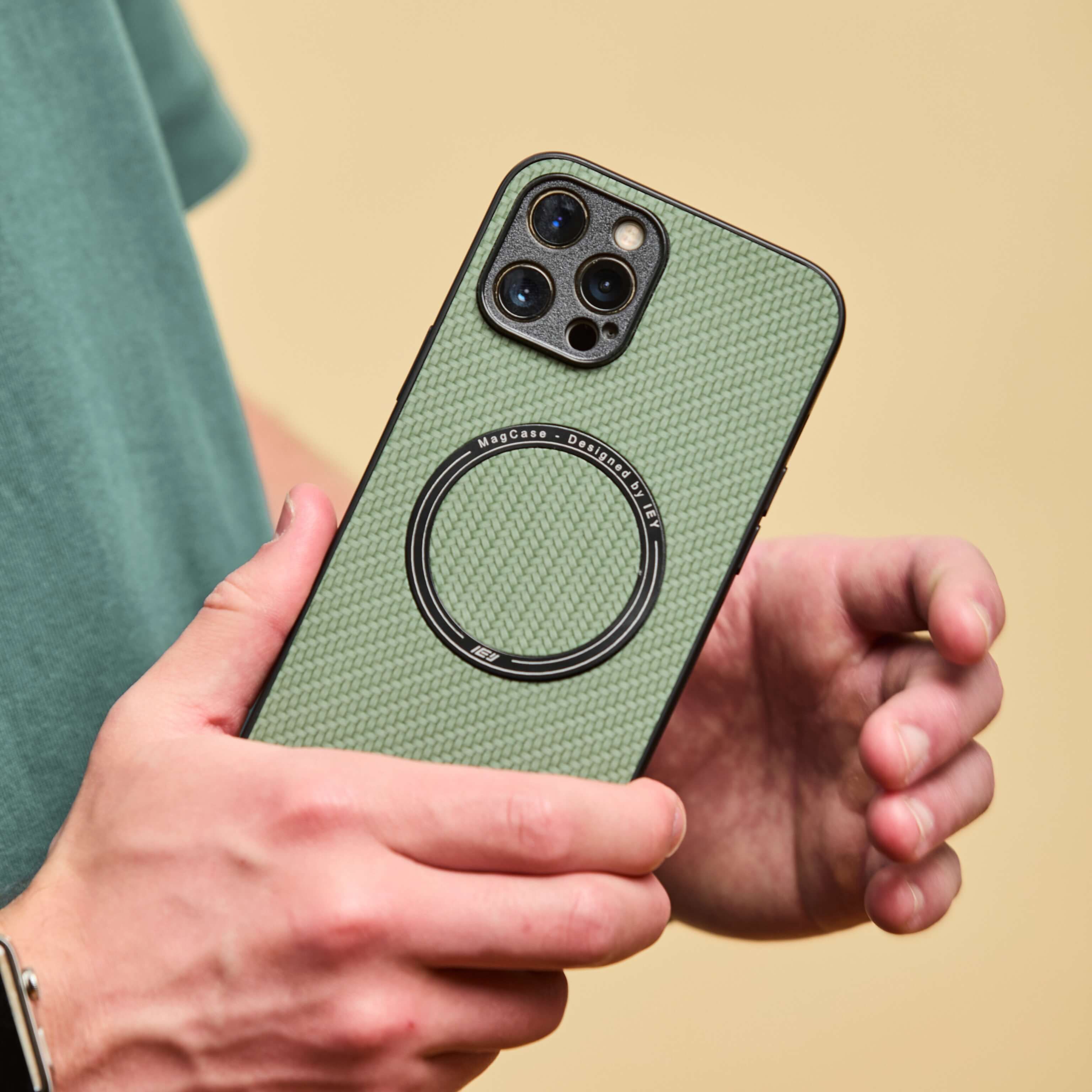 Funda MagSafe verde con textura de carbono sostenida por un hombre de remera verde, en plano detalle sobre fondo beige #color_verde