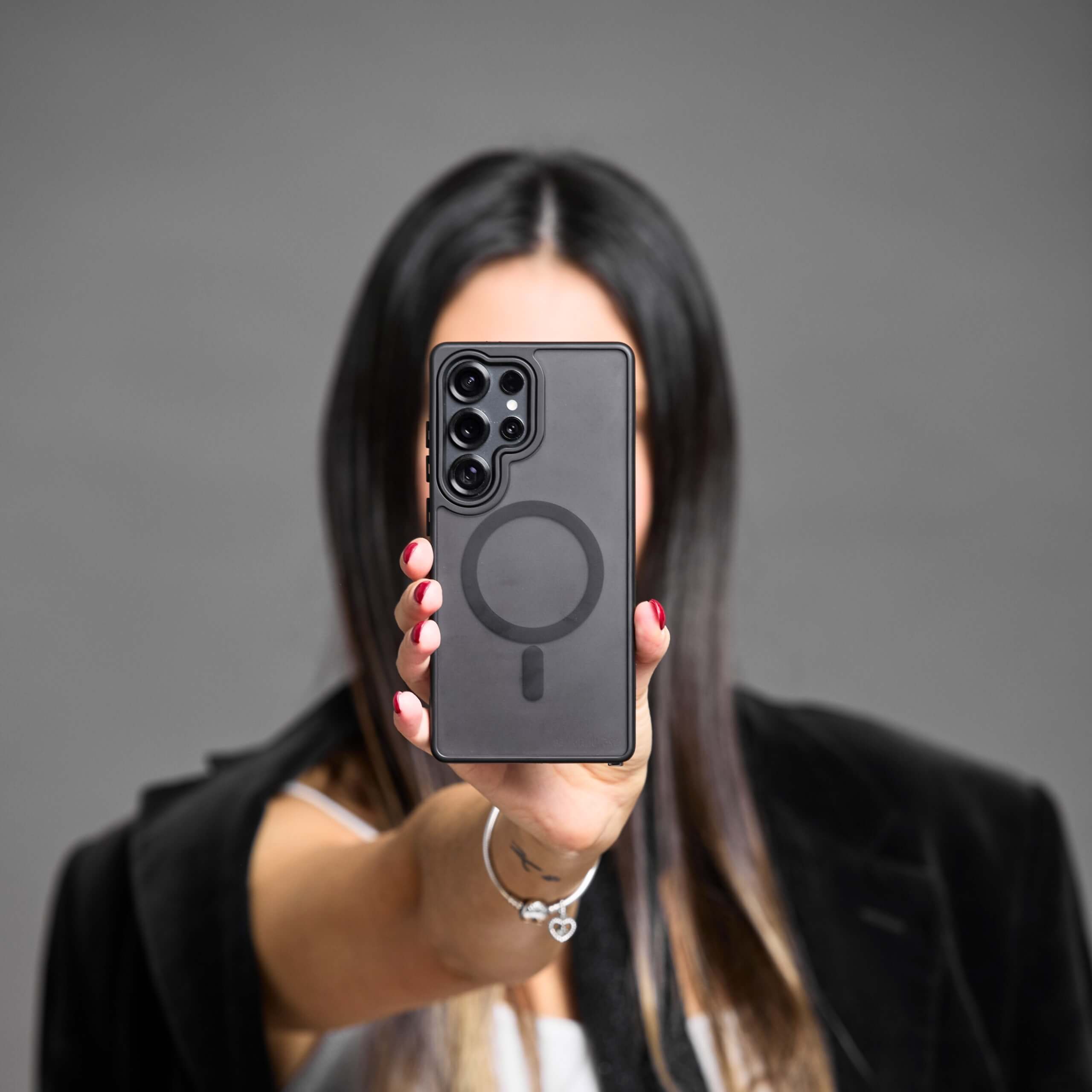 Mujer mostrando un Samsung Galaxy con funda MagSafe negra, vista trasera centrada.