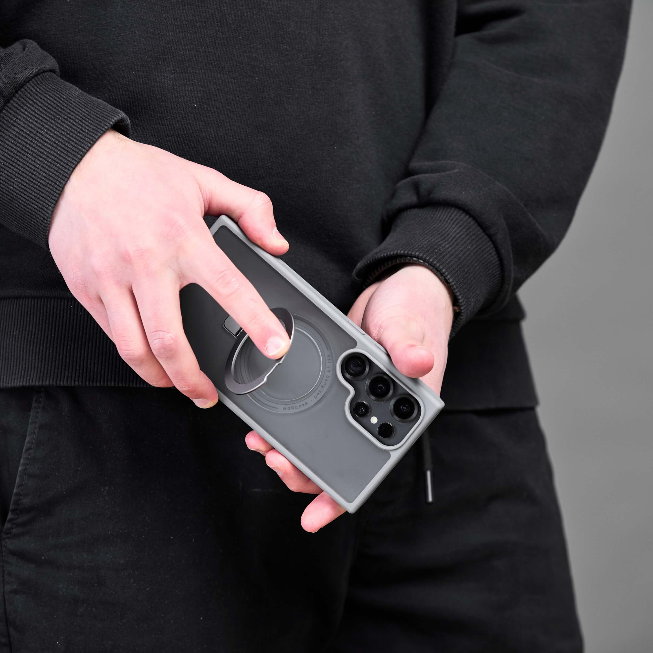 Dos personas mostrando la funda con aro magnético en color negro, sosteniendo el teléfono Samsung S25 Ultra con MagSafe. #color_gris