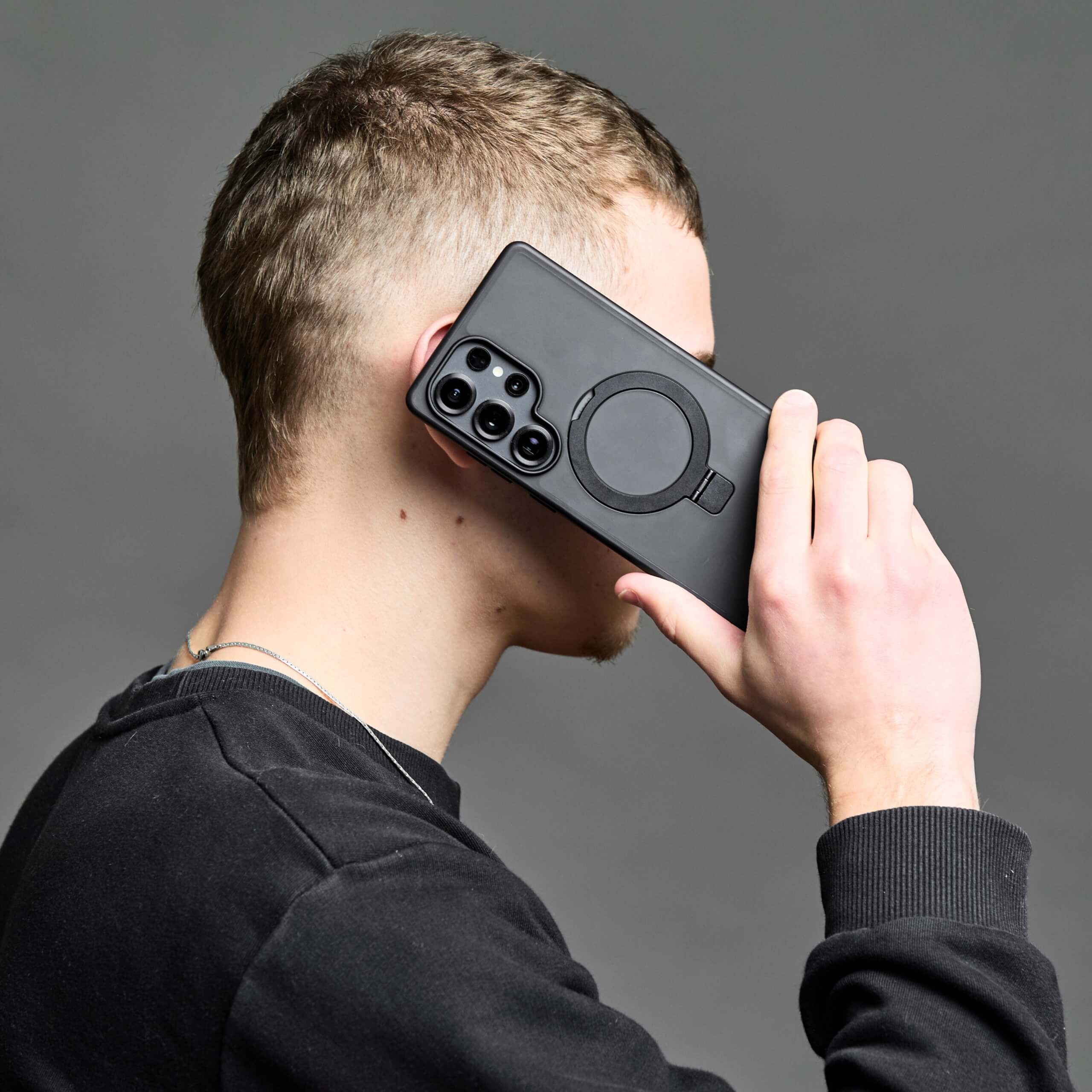 Hombre hablando por teléfono con funda Samsung MagSafe con aro magnético, fondo gris oscuro. #color_negro