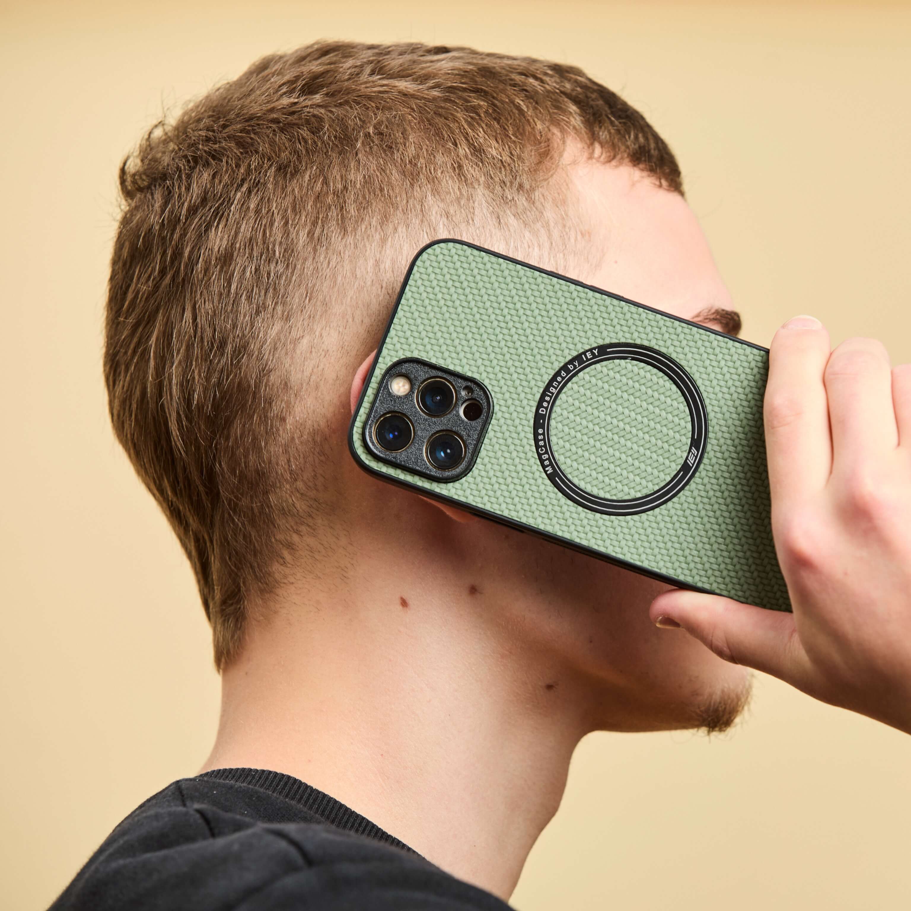 Funda MagSafe verde con textura tipo carbono, en uso durante una llamada, sostenida por un hombre de perfil con remera negra #color_verde