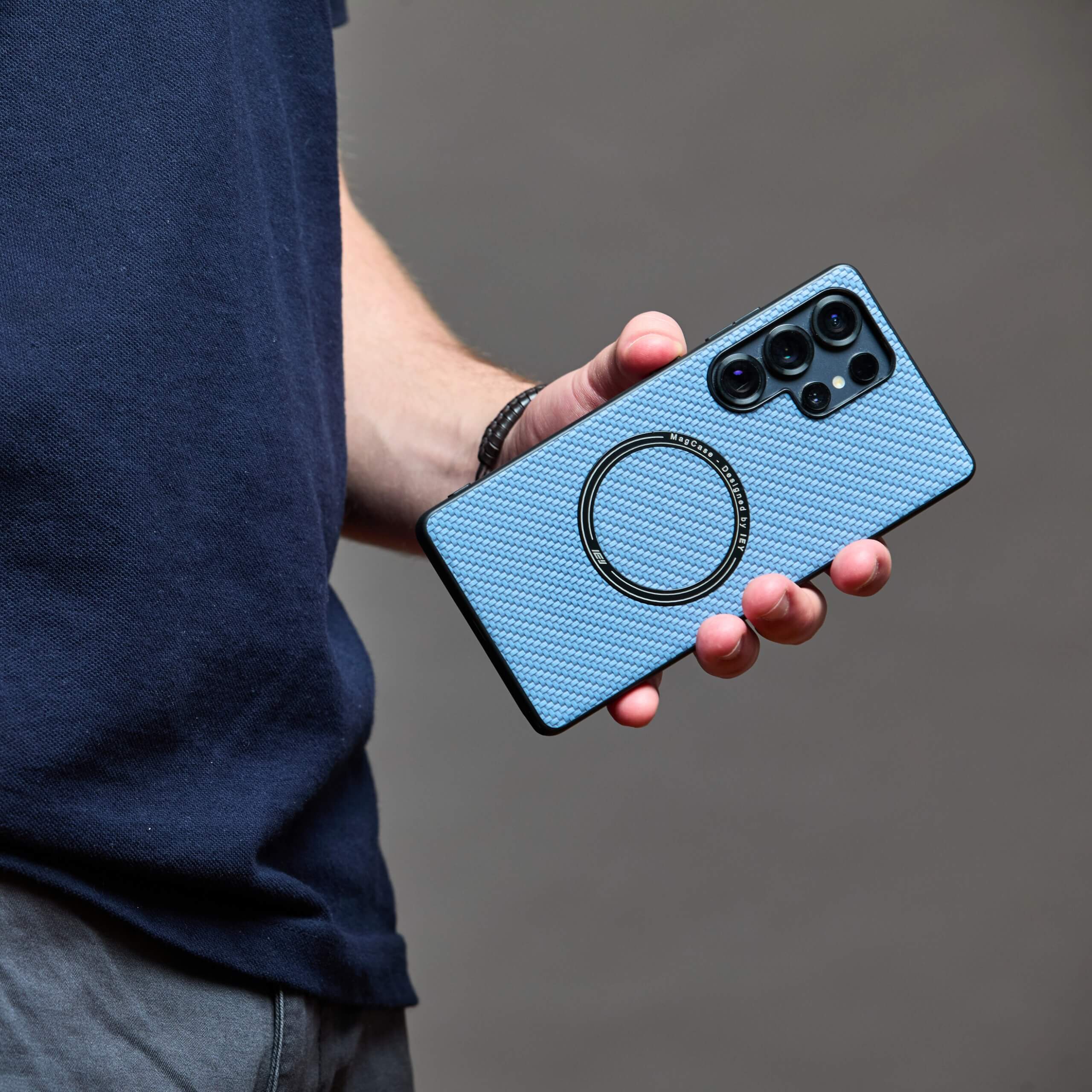 Joven sosteniendo un Samsung con funda MagSafe azul contra su oreja, en perfil izquierdo, fondo beige liso #color_azul