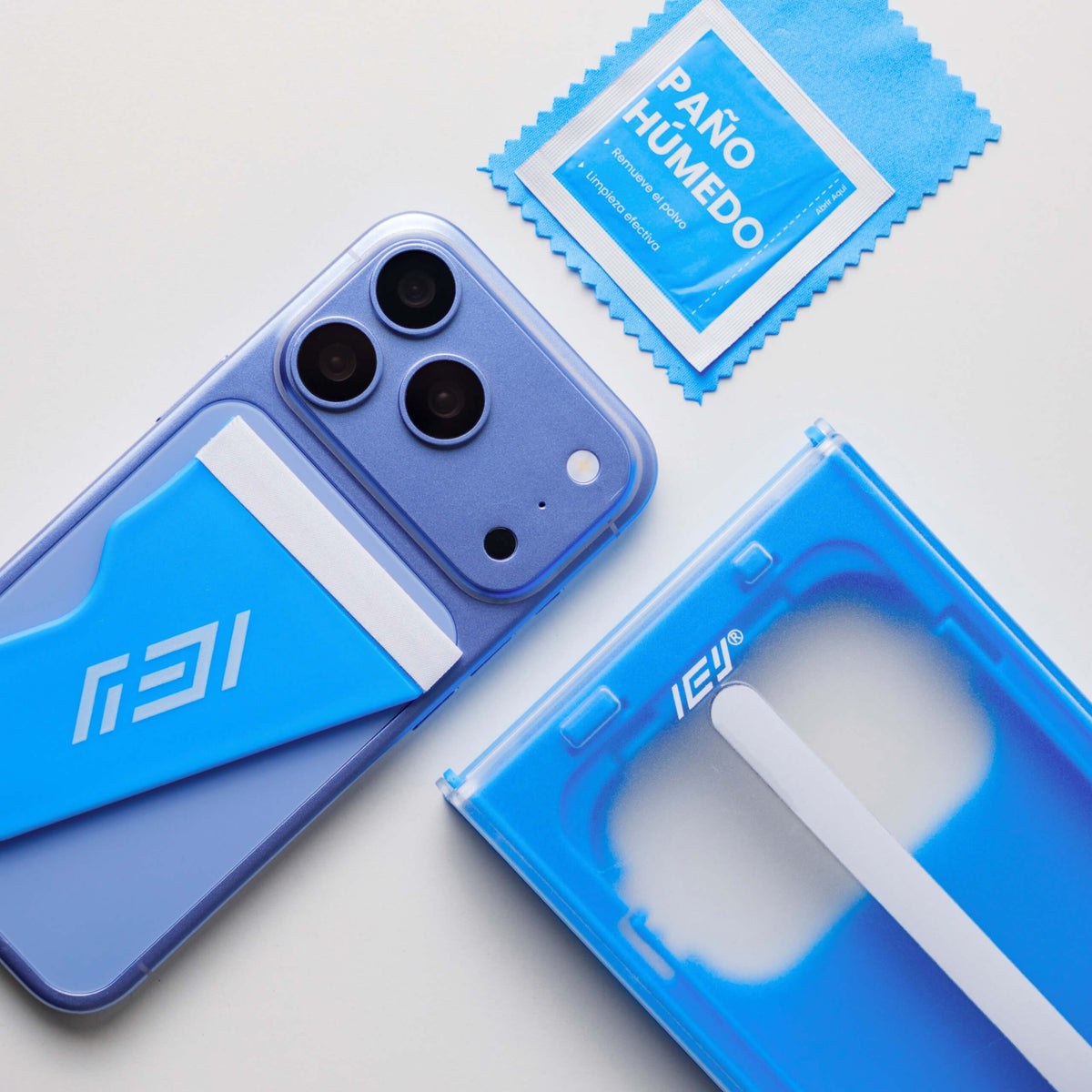 Detalle del kit ApplyFit™ de IEY® junto a un iPhone, con aplicador de vidrio templado, paño húmedo y microfibra de limpieza.