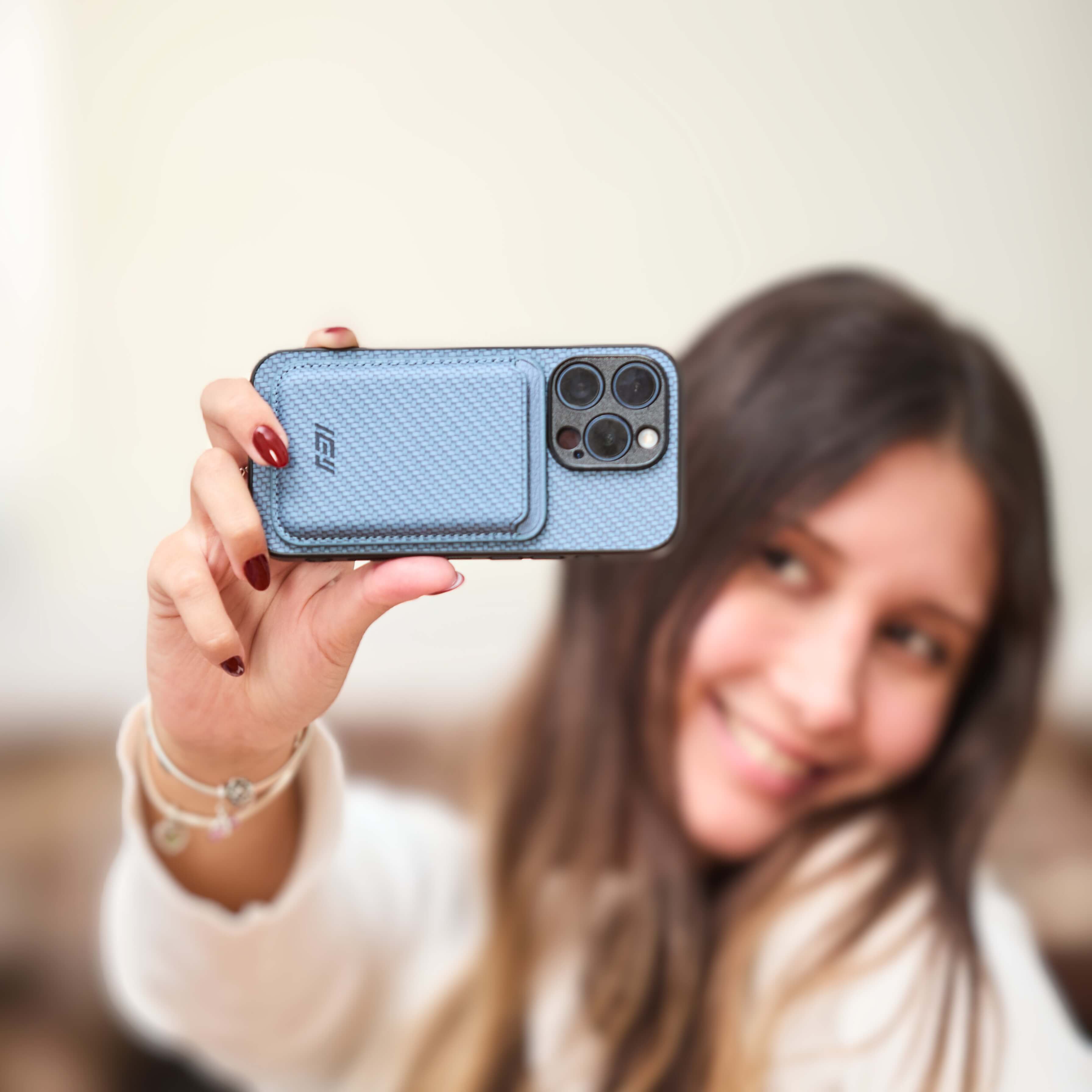 Funda IEY color azul con billetera MagSafe en primer plano, sostenida por una persona sonriendo en segundo plano desenfocado