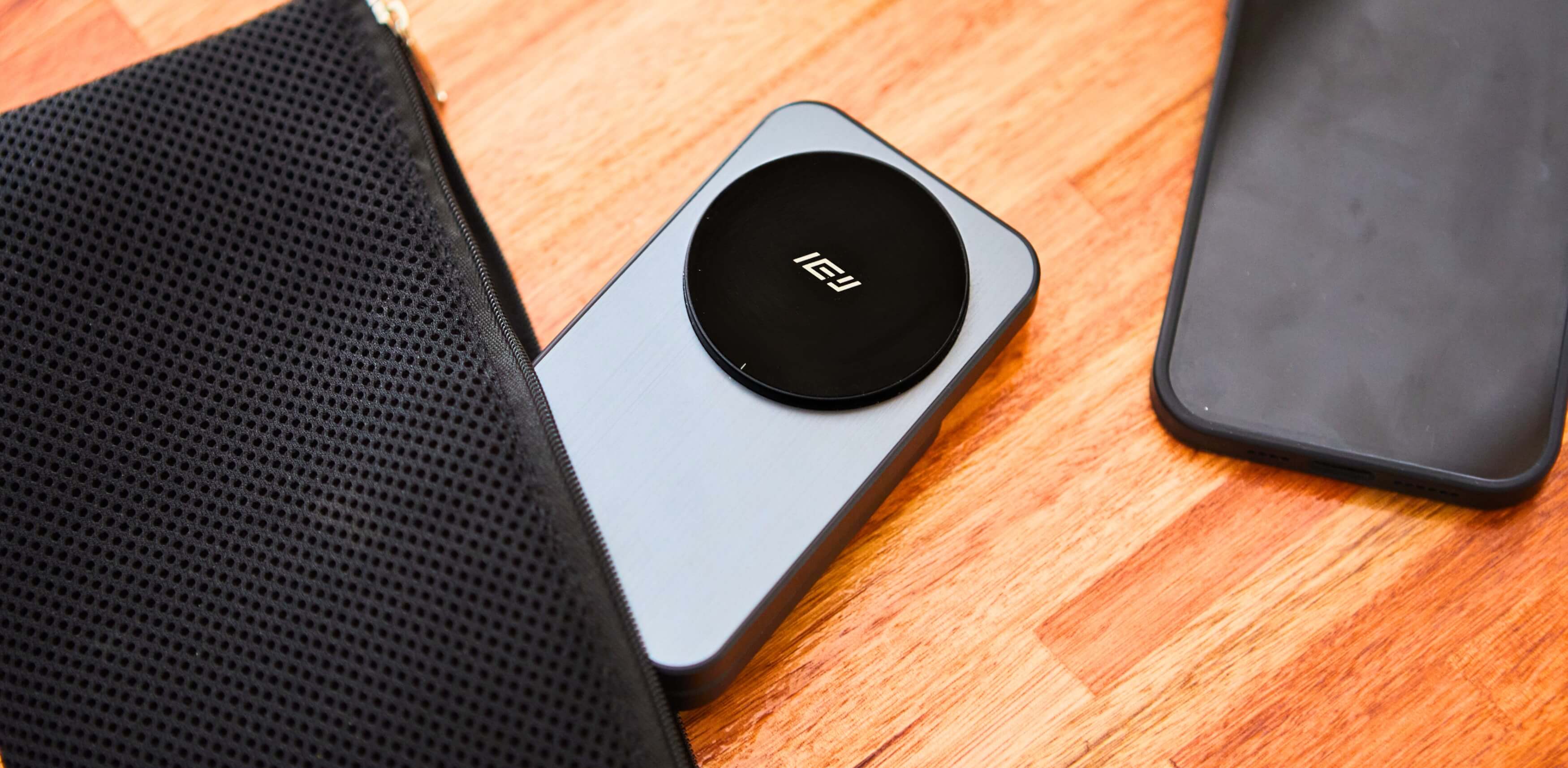Cargador inalámbrico portátil IEY sobre superficie de madera, junto a funda negra y estuche deportivo.