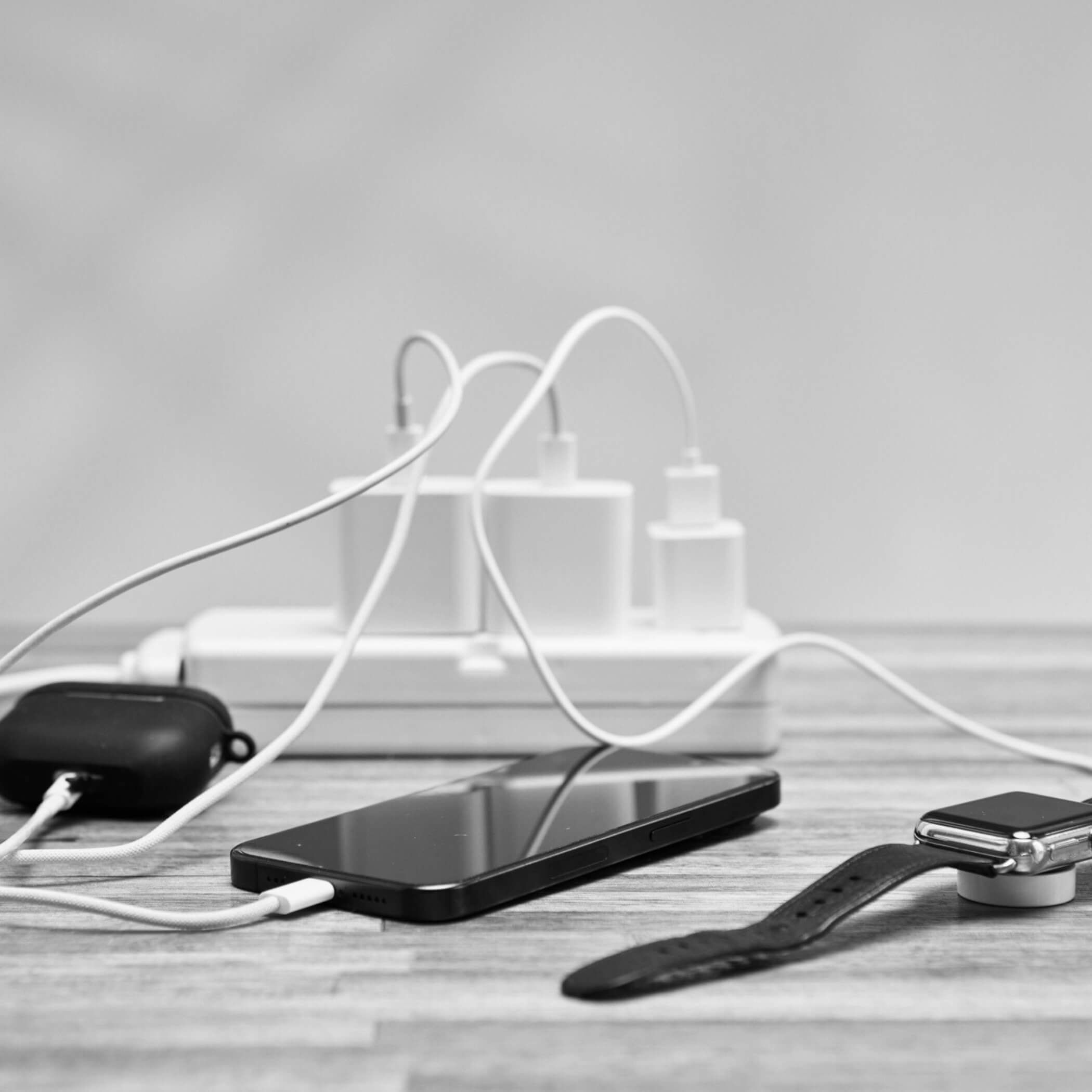 Múltiples dispositivos cargando con cables en regleta eléctrica: iPhone, Apple Watch y auriculares, mostrando desorden por cargadores tradicionales