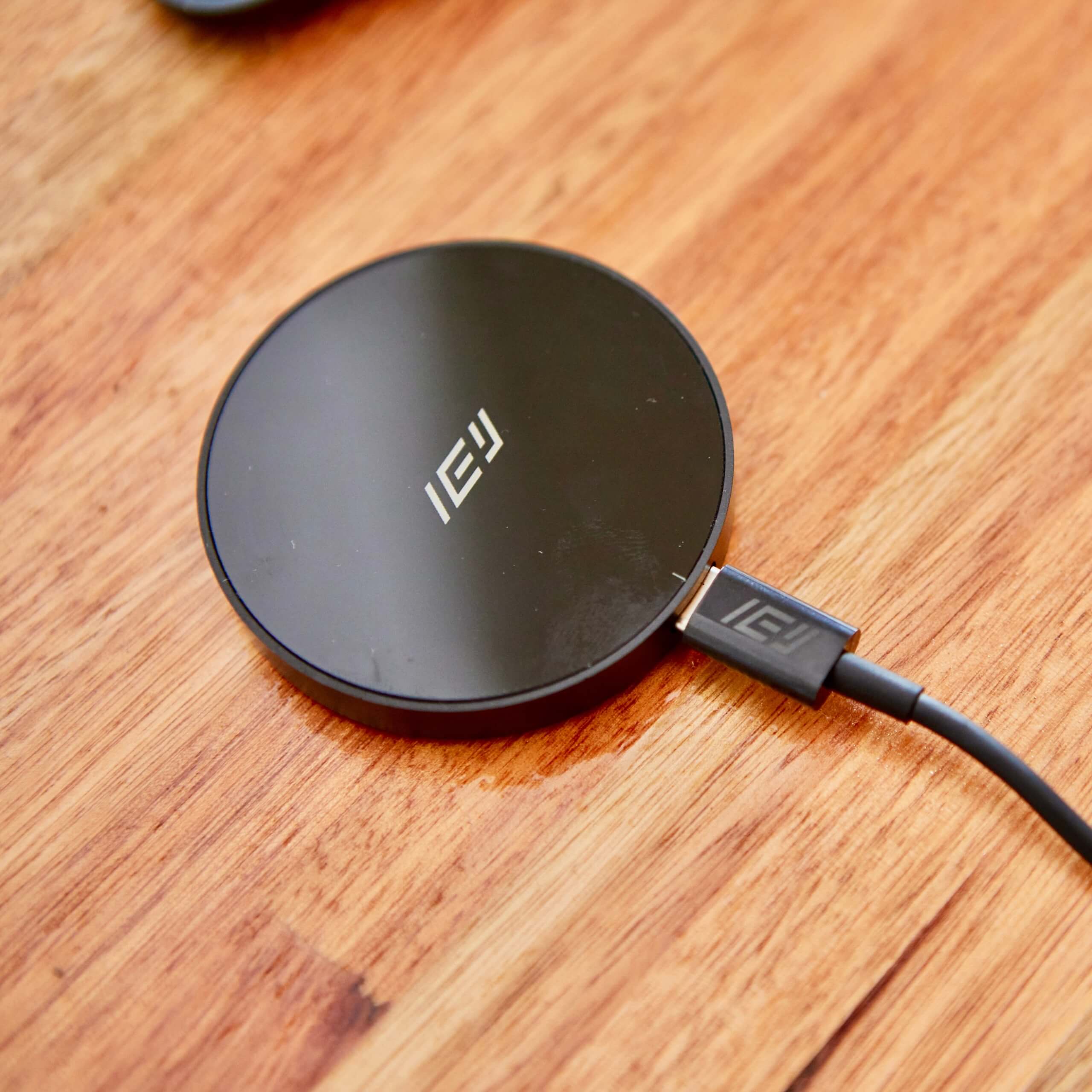 Base de carga inalámbrica negra marca IEY conectada mediante cable USB-C sobre superficie de madera