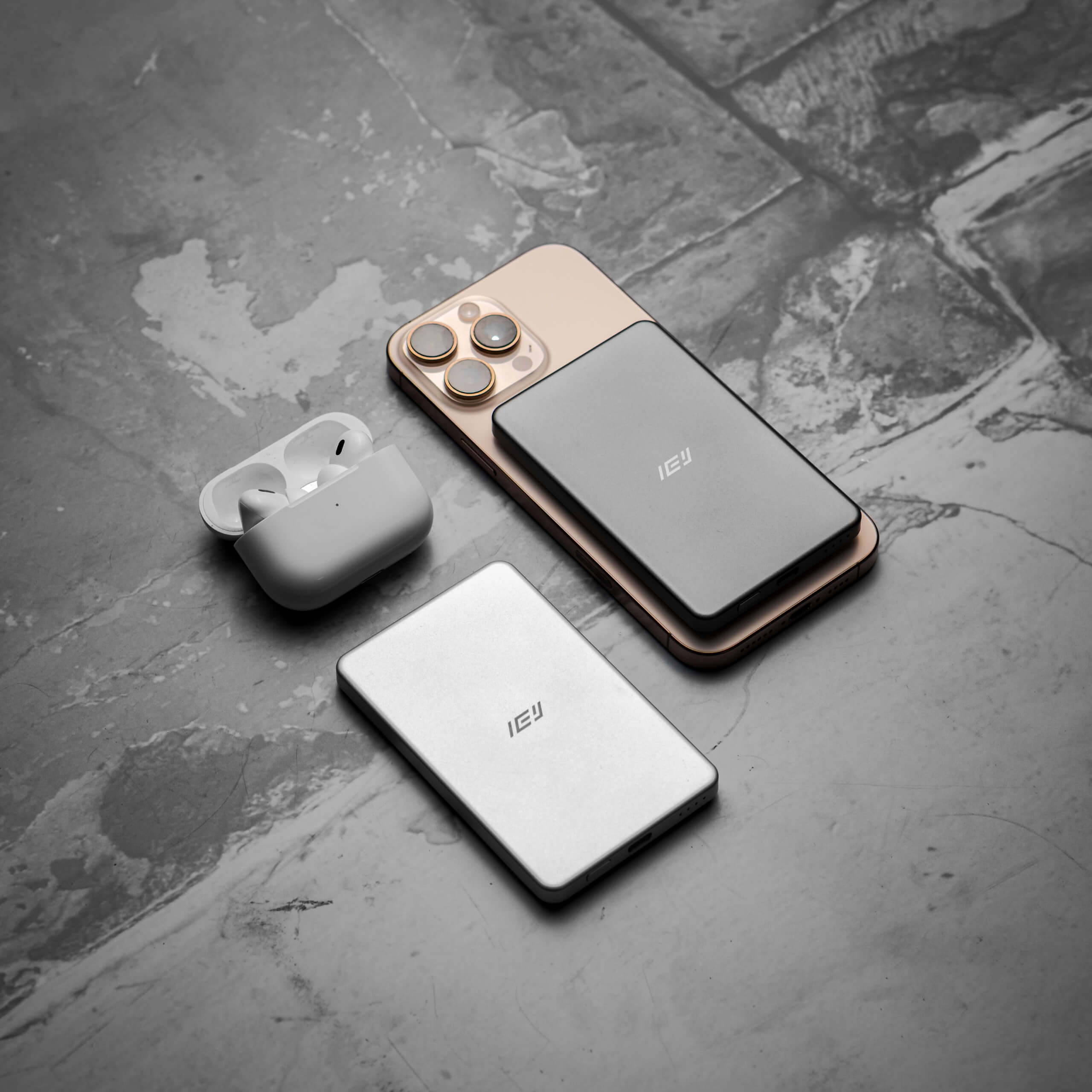 Power Bank MagSafe ultrafino IEY en color gris y blanco, compatible con iPhone y AirPods, diseño minimalista sobre superficie gris.