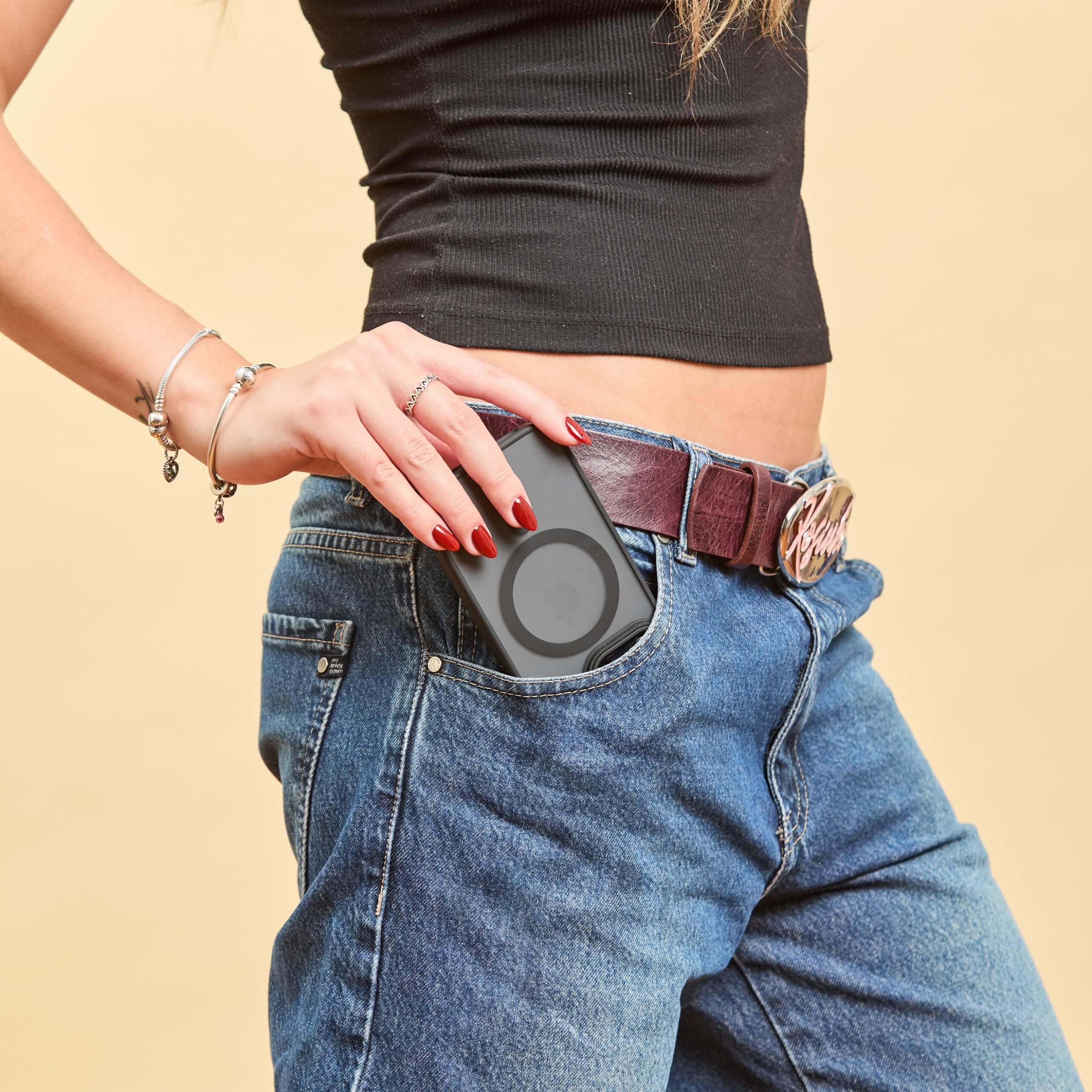 Funda MagSafe negra siendo guardada en el bolsillo delantero de un jean, sostenida con una mano femenina