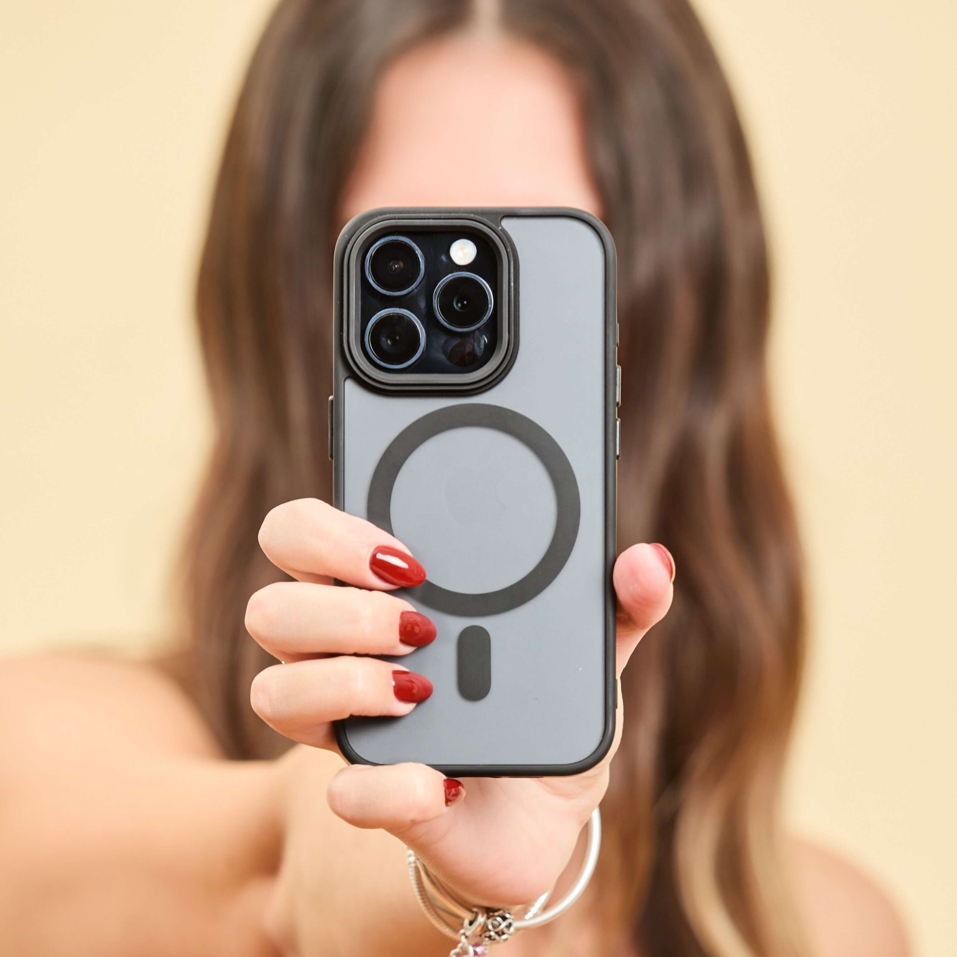 Funda MagSafe negra para iPhone sostenida frontalmente por una persona, con aro imantado