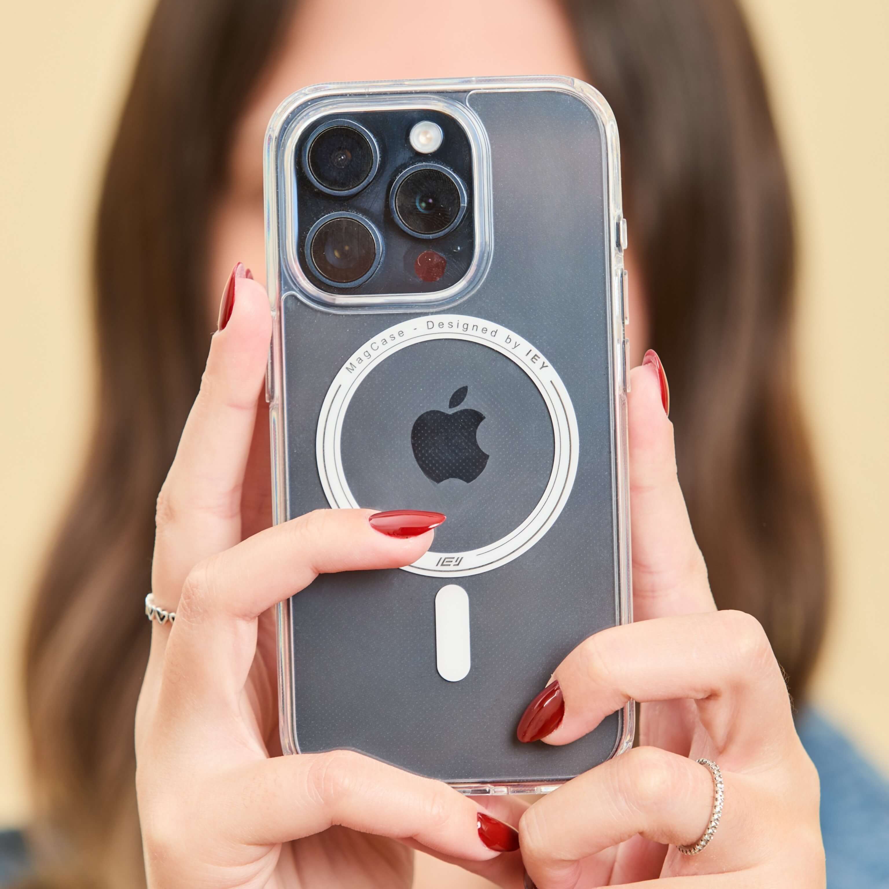 Funda MagSafe transparente para iPhone sostenida frontalmente por una persona, con aro imantado y marca IEY visible