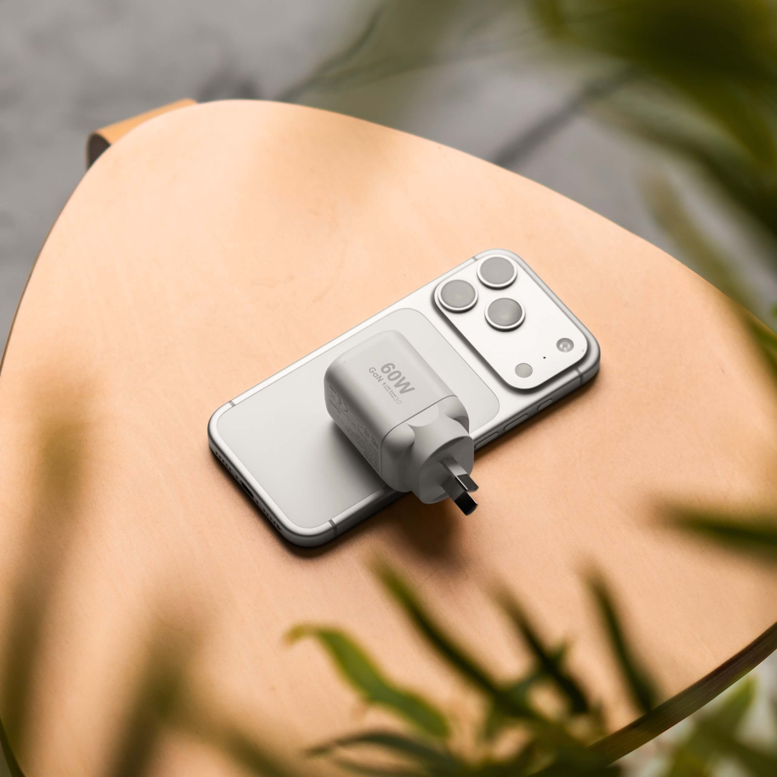 Cargador de pared GaN USB-C 60W IEY® blanco sobre smartphone en mesa de madera