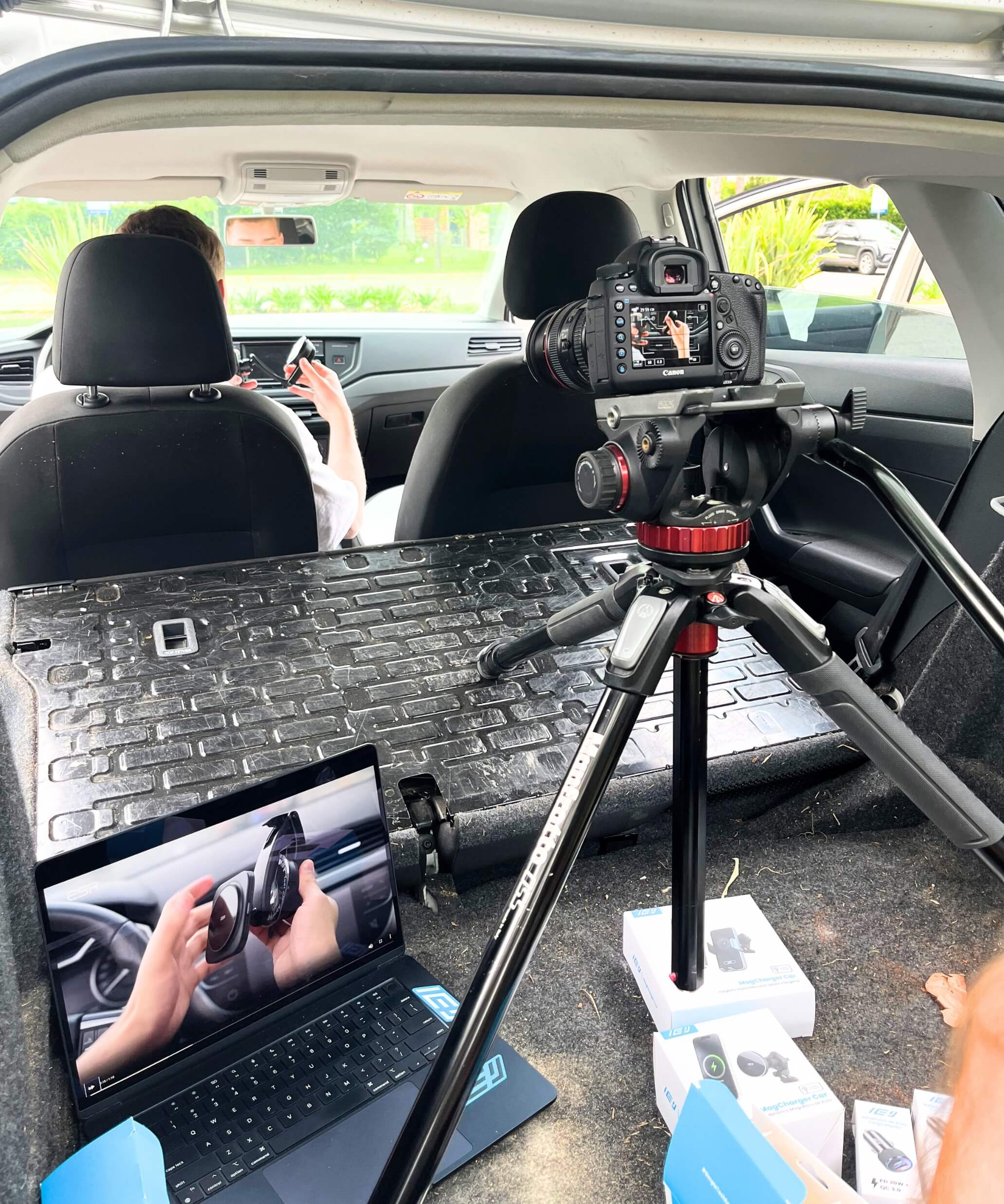 Cámara profesional grabando instalación de accesorio IEY en auto, vista desde el baúl con laptop mostrando previa del video