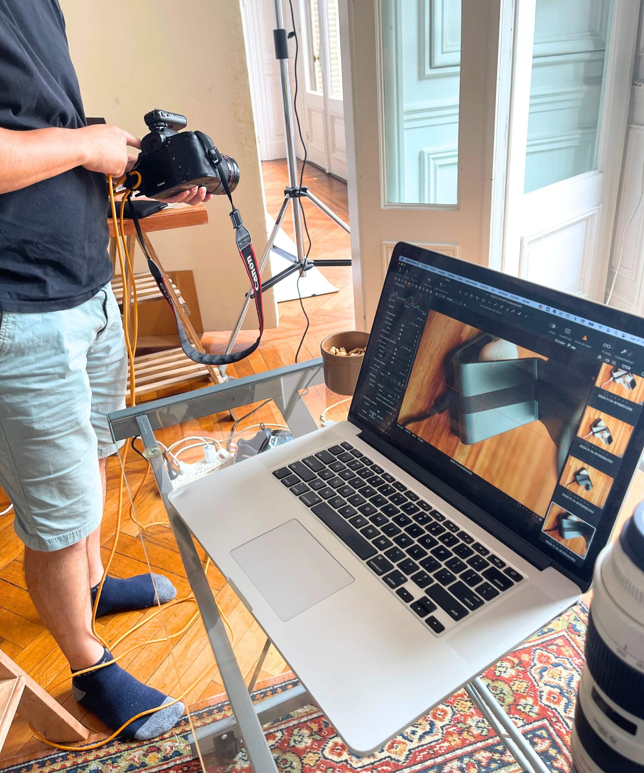 Laptop con sesión fotográfica de producto IEY en pantalla, mientras fotógrafo revisa capturas conectando cámara profesional en estudio