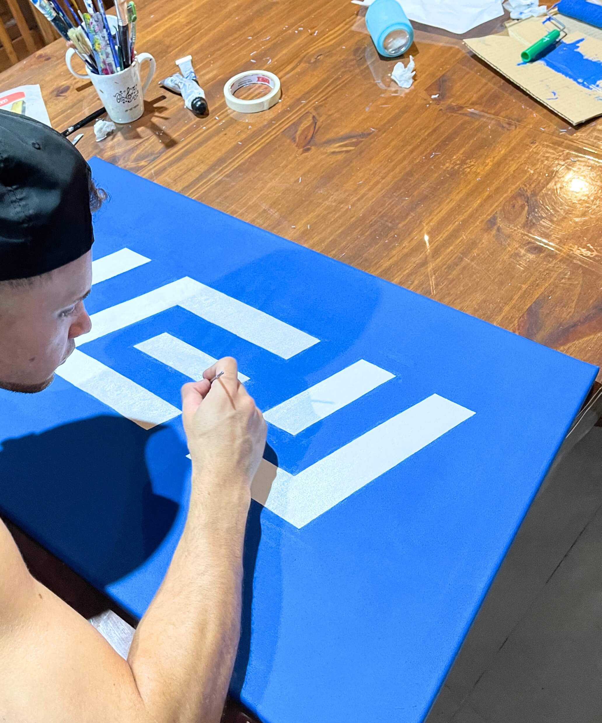 Persona pintando a mano el logotipo de IEY sobre lienzo azul, mostrando el proceso creativo y artesanal detrás de la identidad visual de la marca