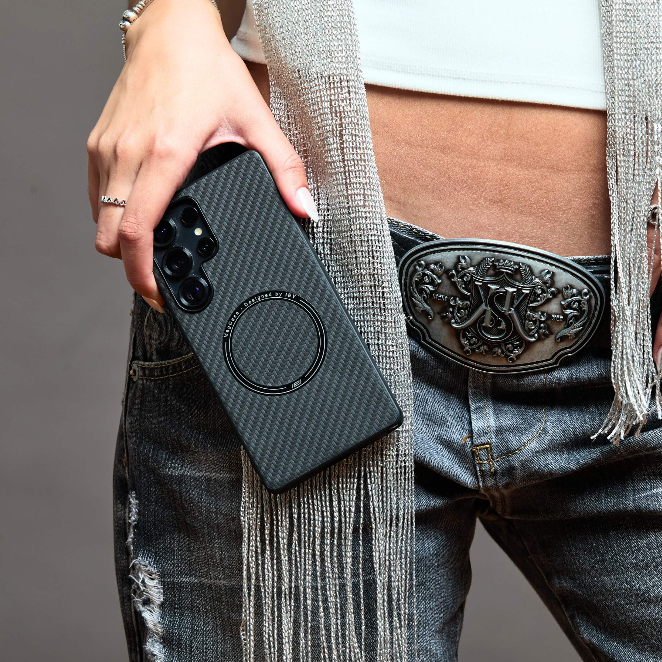 Mujer sosteniendo su teléfono frente al rostro con funda MagSafe Samsung negra de textura carbono, sobre fondo beige #color_negro