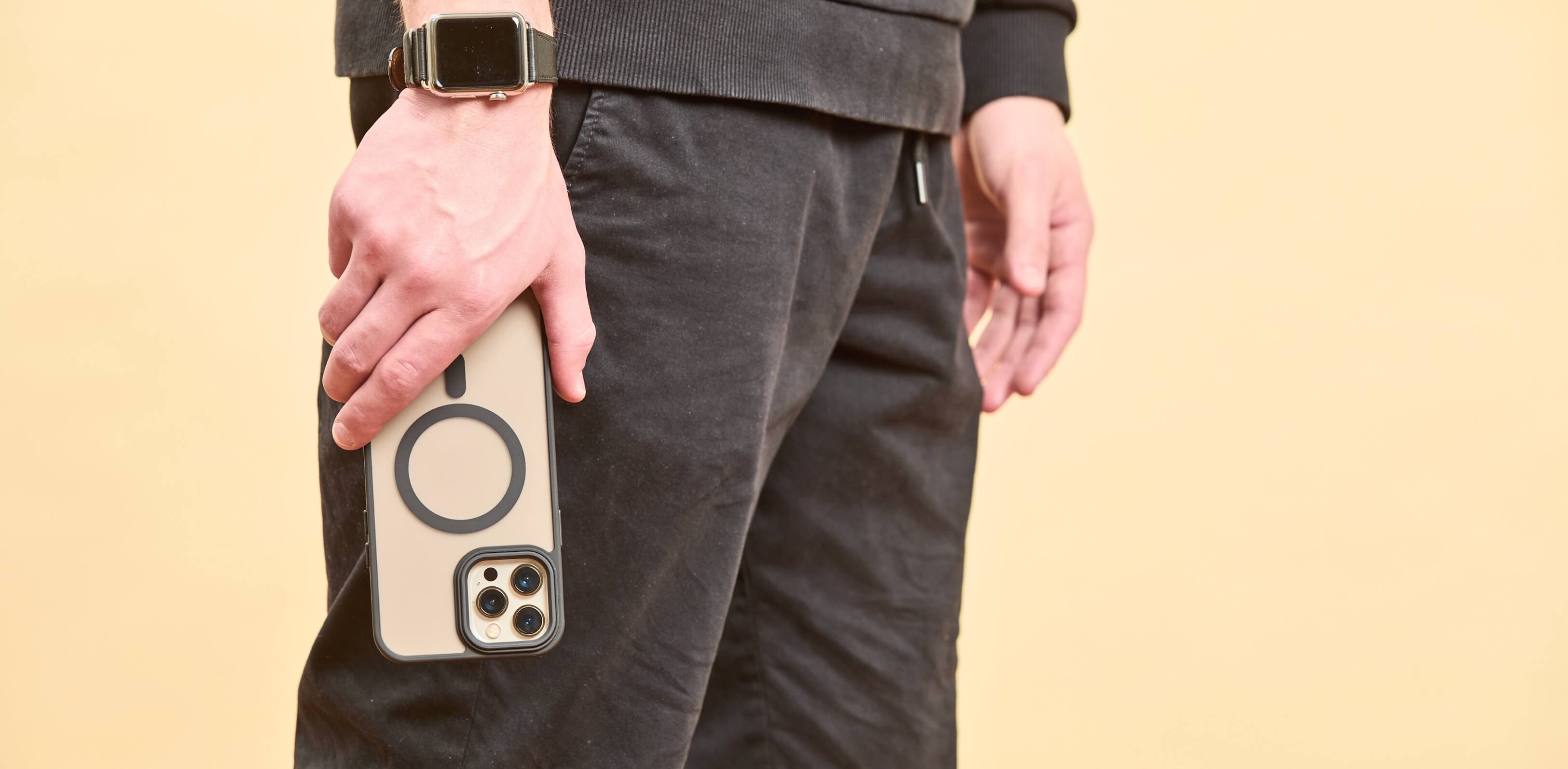 Hombre de negro sosteniendo un iPhone con funda MagSafe mate y bordes negros, al costado de su pierna