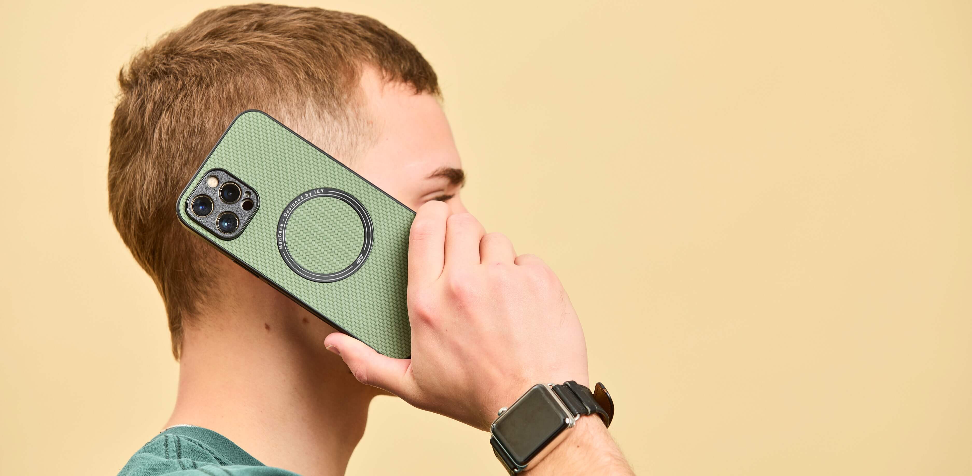 Hombre usando funda verde con anillo MagSafe de IEY mientras sostiene el teléfono en la oreja sobre fondo beige