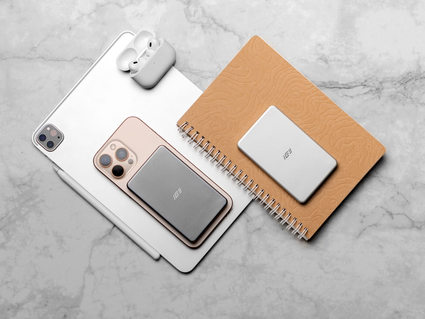 Batería inalámbrica MagSafe IEY ultrafina en color gris y blanco, junto a iPhone, iPad y AirPods, estilo lifestyle sobre mesa de mármol.