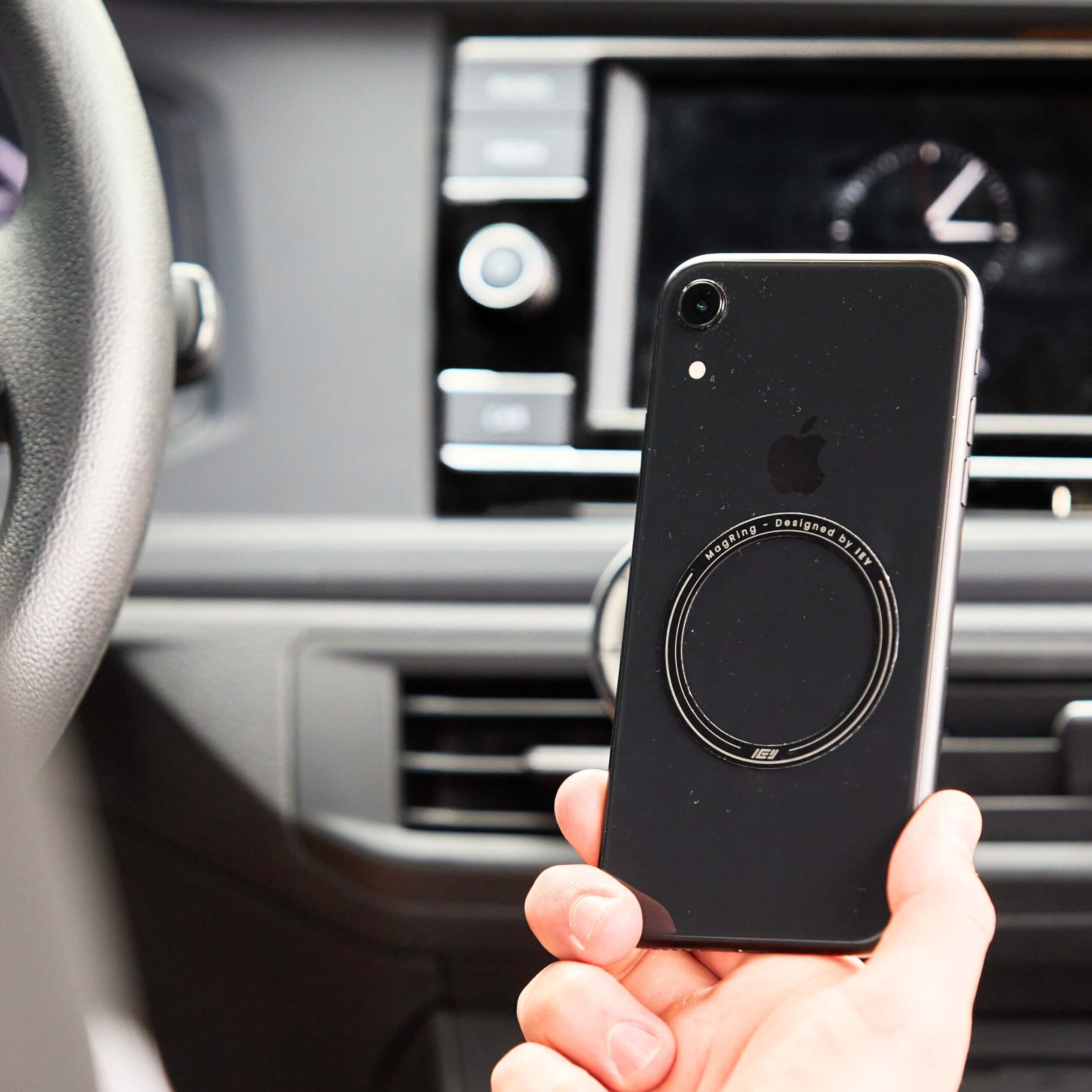 Teléfono con anillo magnético IEY MagRing adherido en la parte trasera, mostrando compatibilidad con MagSafe dentro del auto