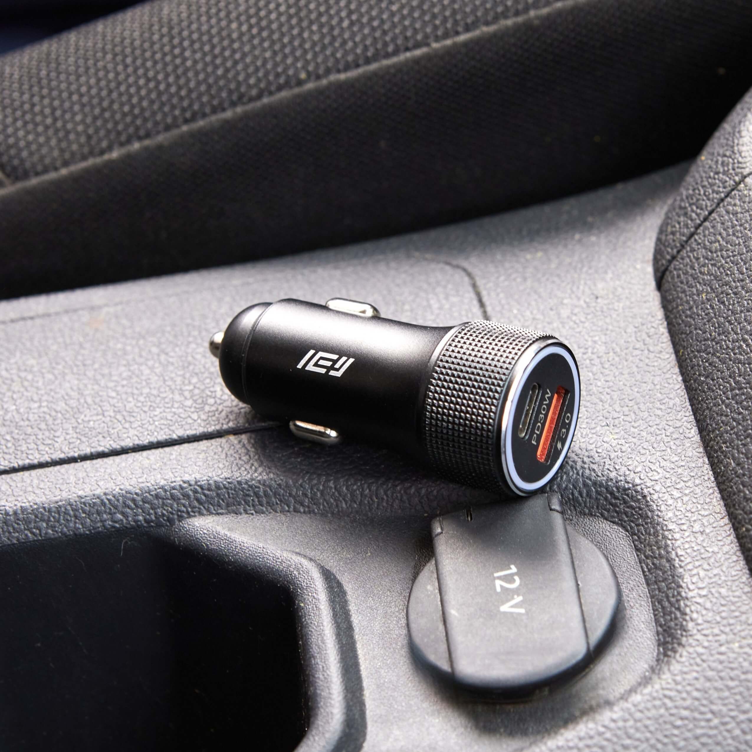 Cargador de auto IEY de 30W con doble puerto USB-C y USB-A apoyado junto a toma de 12V en la consola central del vehículo
