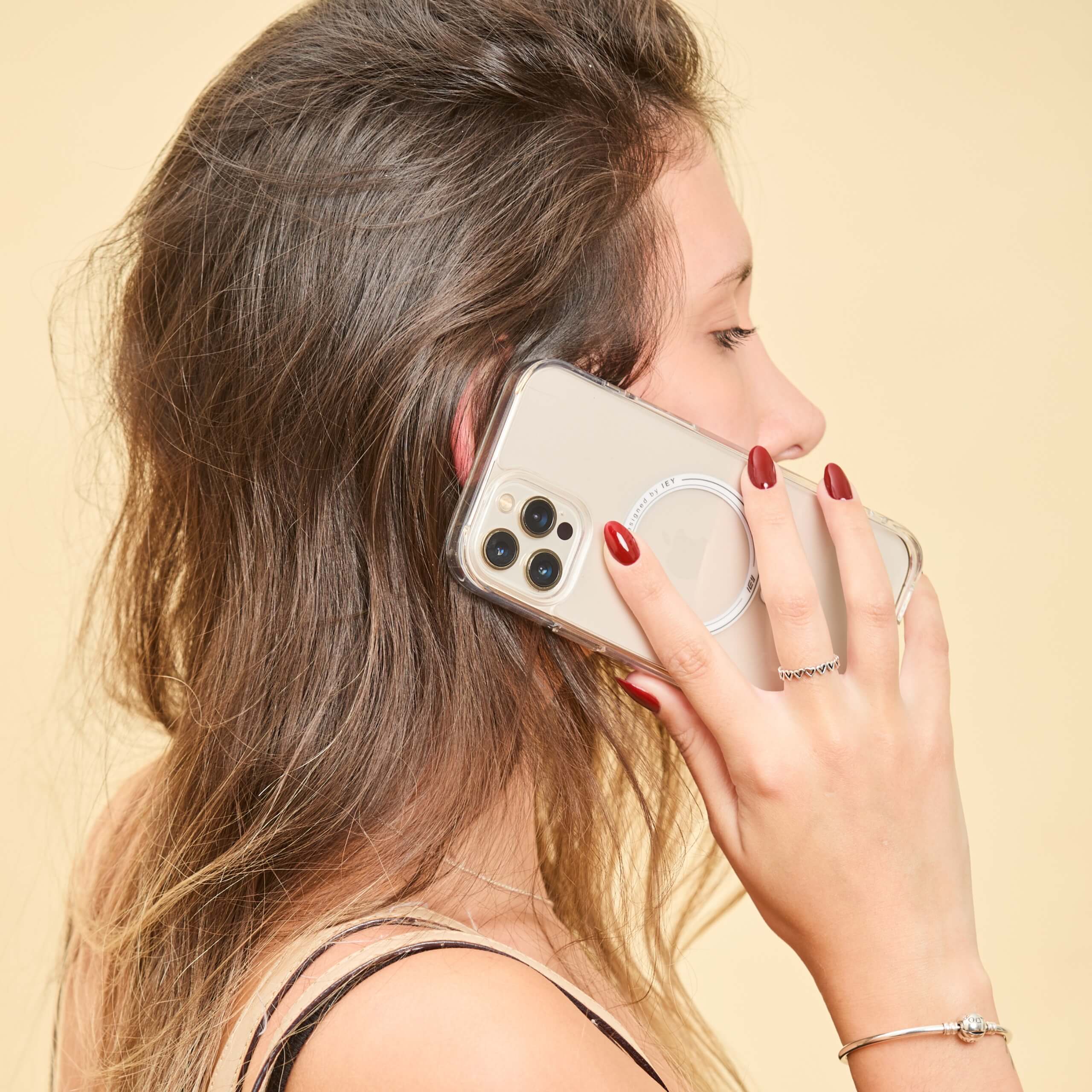 Mujer en llamada con iPhone protegido por funda MagSafe transparente, vista lateral con estilo casual y bolso al hombro