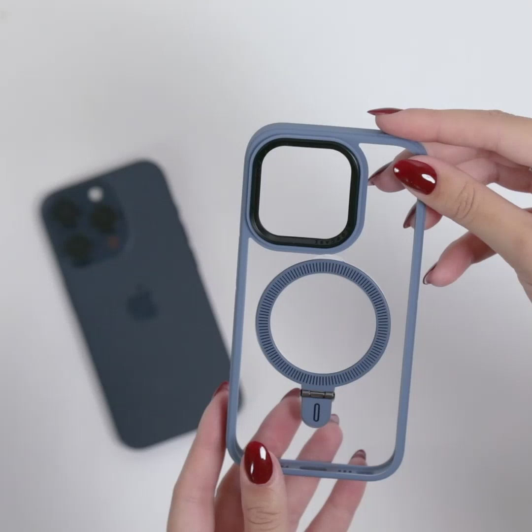 Manos femeninas mostrando funda MagSafe azul translúcida con anillo integrado, sobre fondo blanco con un iPhone azul desenfocado al fondo. 