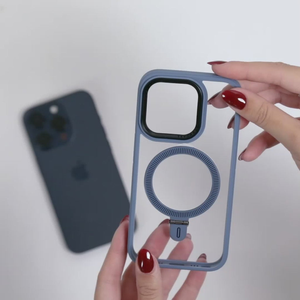 Manos femeninas mostrando funda MagSafe azul translúcida con anillo integrado, sobre fondo blanco con un iPhone azul desenfocado al fondo. 