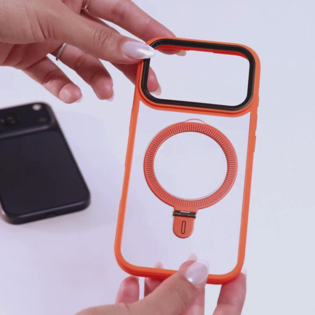 Manos femeninas mostrando funda MagSafe azul translúcida con anillo integrado, sobre fondo blanco con un iPhone naranja desenfocado al fondo. 